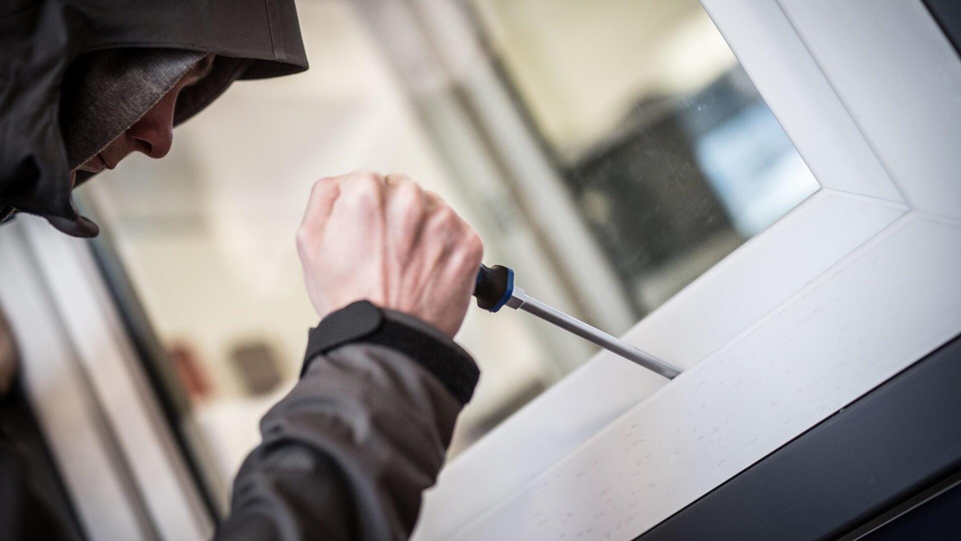 Ein Mann hebelt mit einem Schraubenzieher ein Fenster auf.