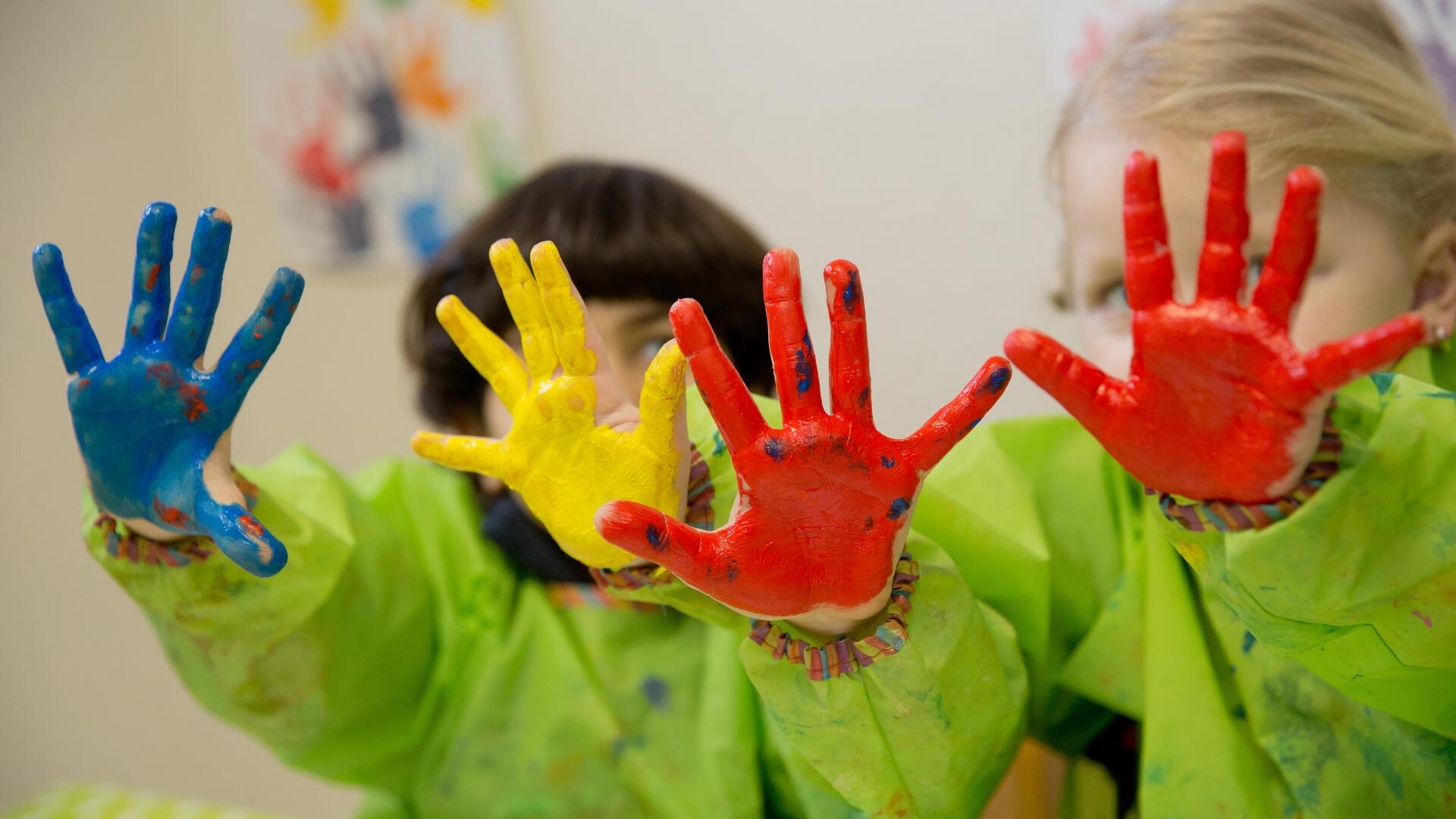 Zwei Kinder haben ihre Finger bemalt und halten ihre Hände in die Kamera.