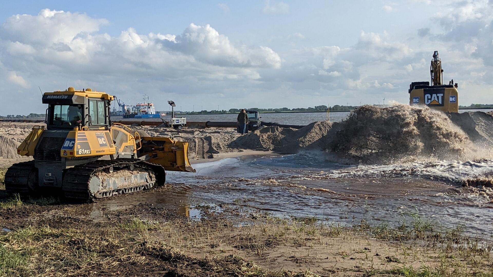 In einem dicken Strahl wird das aus der Weser gewonnen Material an den Strand gespült. Hier verteilen schwere Baumaschinen den Sand und sorgen so für einen verbesserten Küstenschutz.