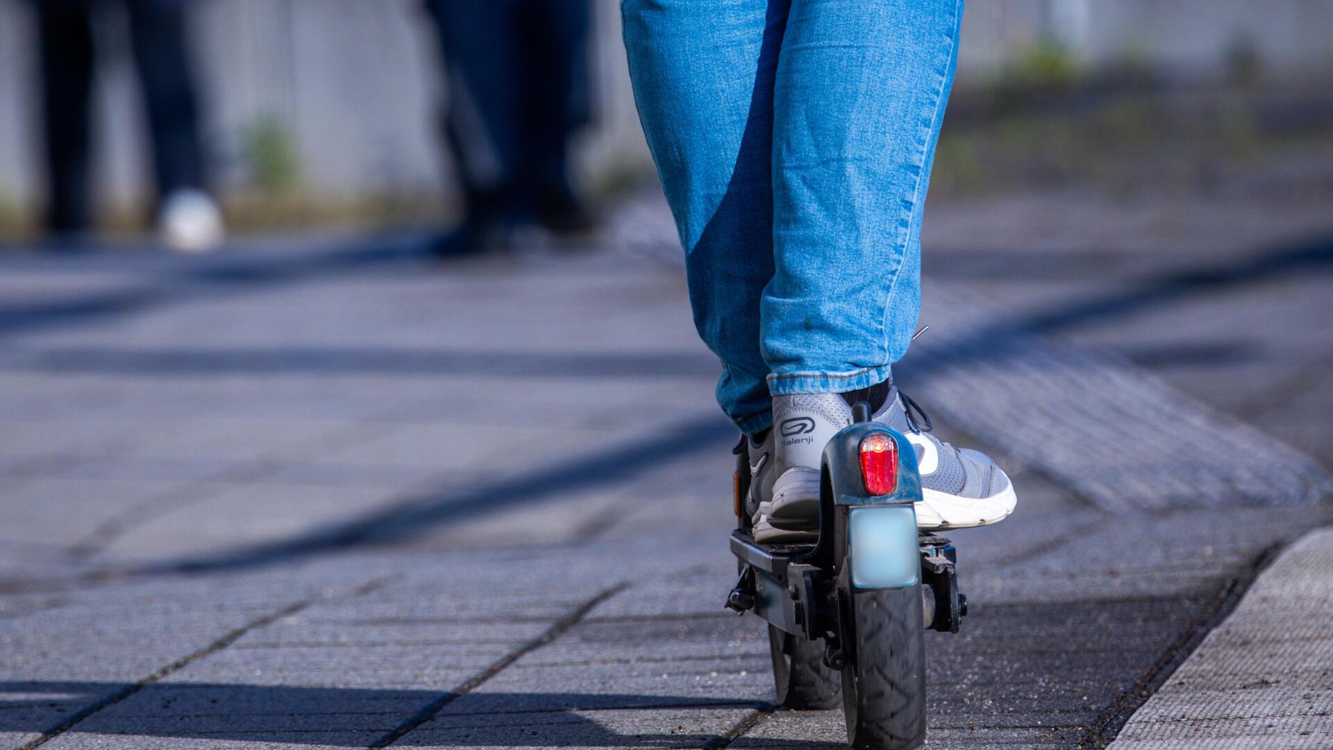 Zwei Beine auf einem E-Scooter sind von hinten zu sehen