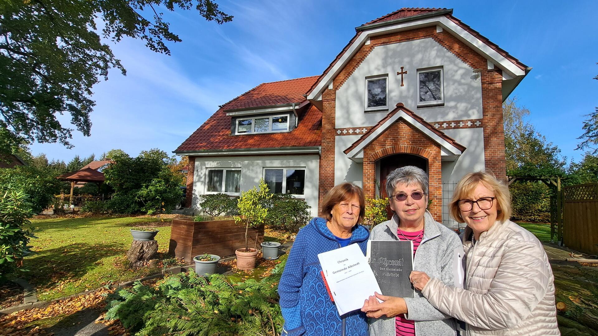 Ingrid Bullwinkel (v.l.), Gerlinde Sawatzki und Edda Goede vor der alten Schule in Albstedt mit der alten Schulchronik und der Übersetzung. 