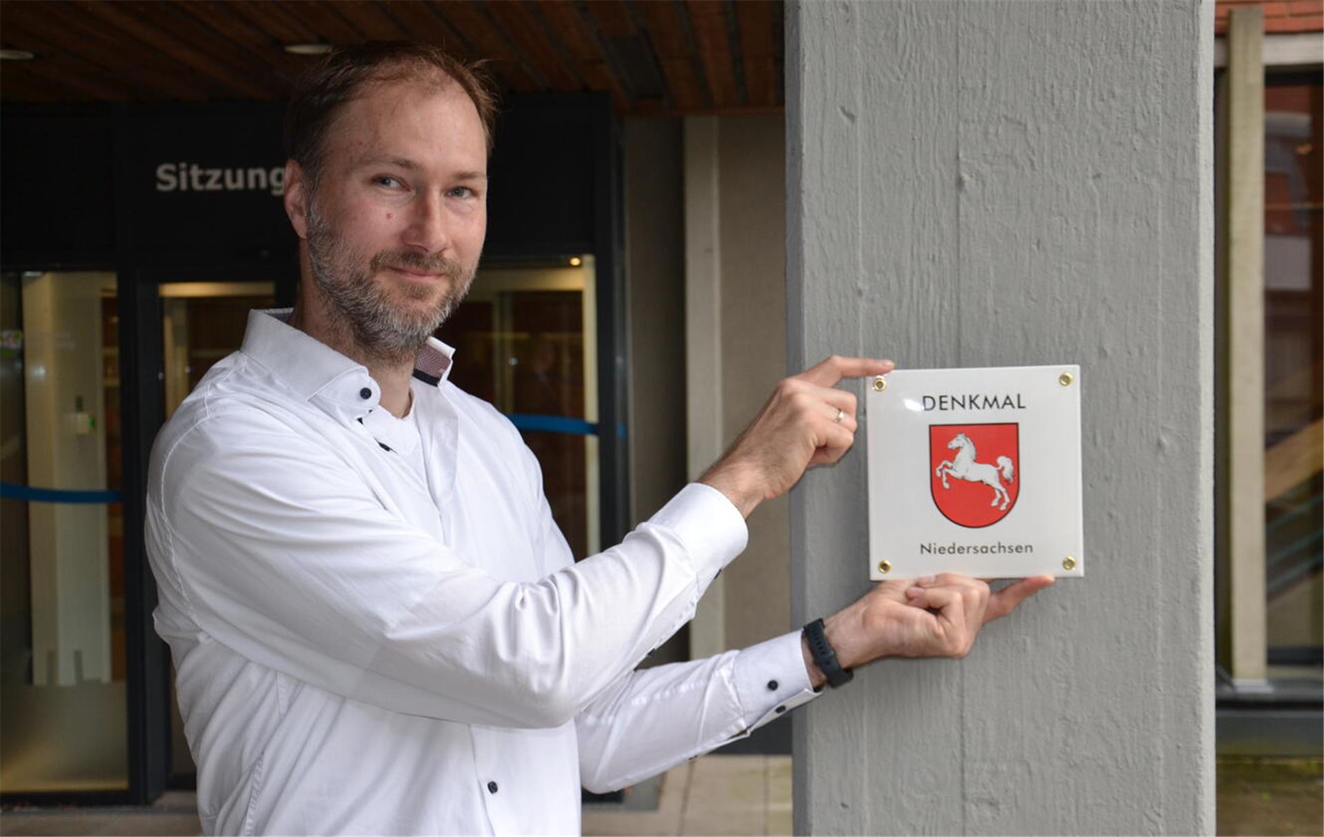 Jan Lubitz vom Landesamt für Denkmalpflege präsentiert das neu gestaltete Schild, dass das Kreishaus in Rotenburg als Denkmal ausweist.