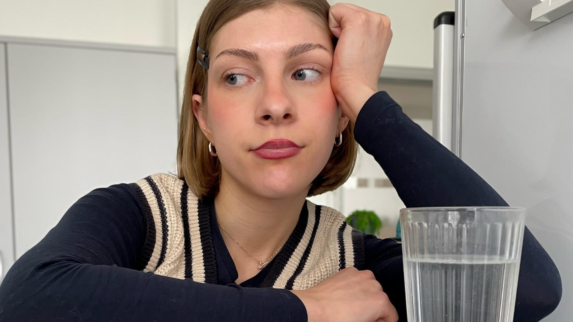 Eine Frau sitzt vor einem Glas mit Wasser.