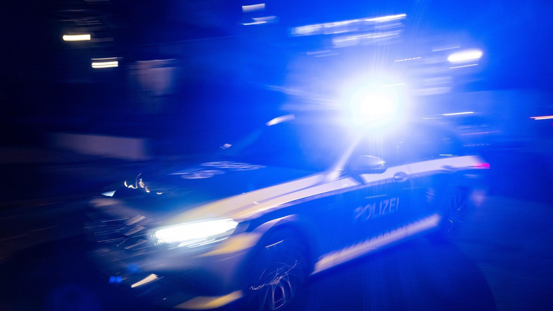 Ein Polizeifahrzeug fährt mit Blaulicht an einem Gebäude vorbei.