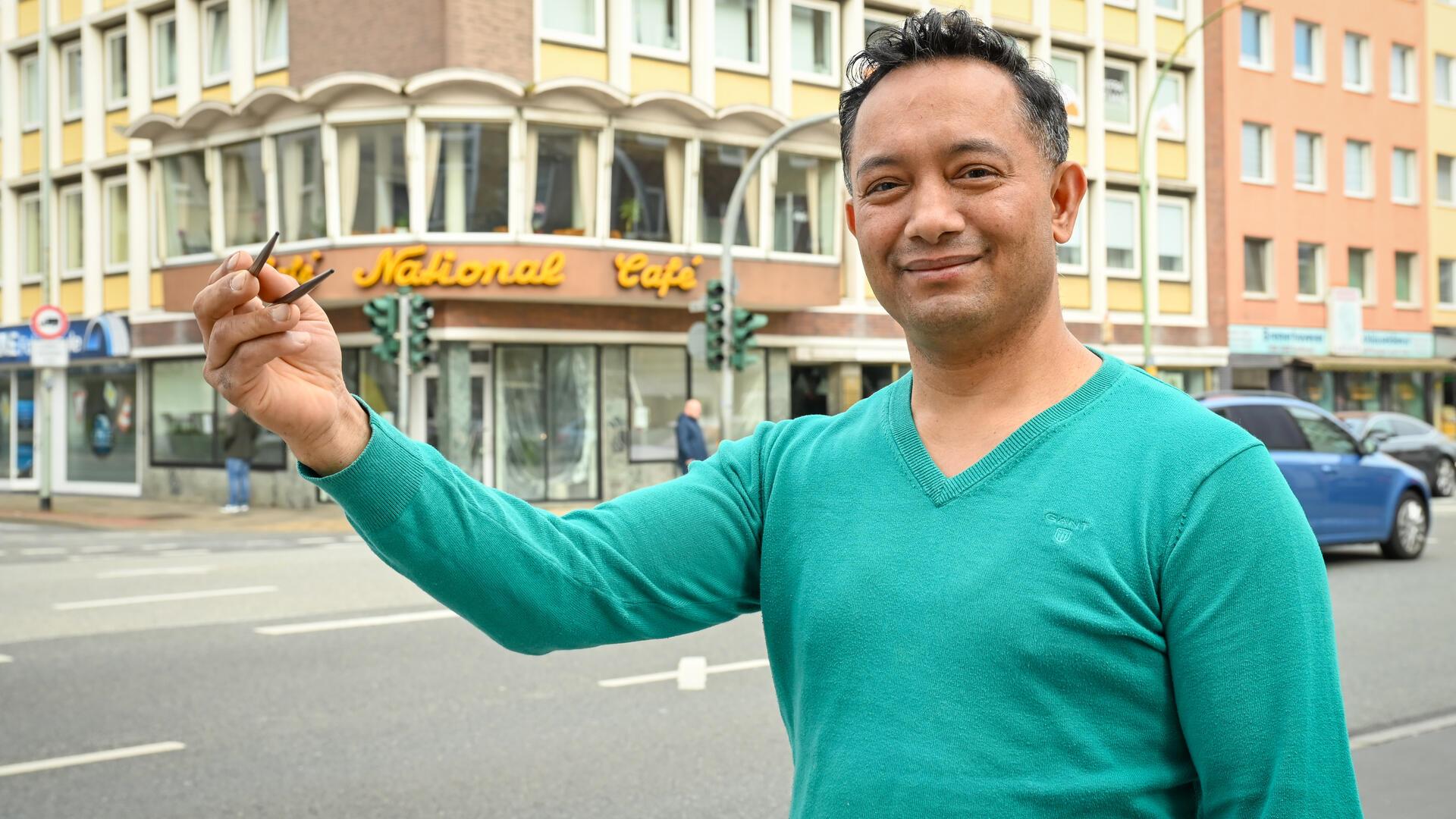 Ein Mann mit grünem Pullover hat zwei Essstäbchen in der Hand