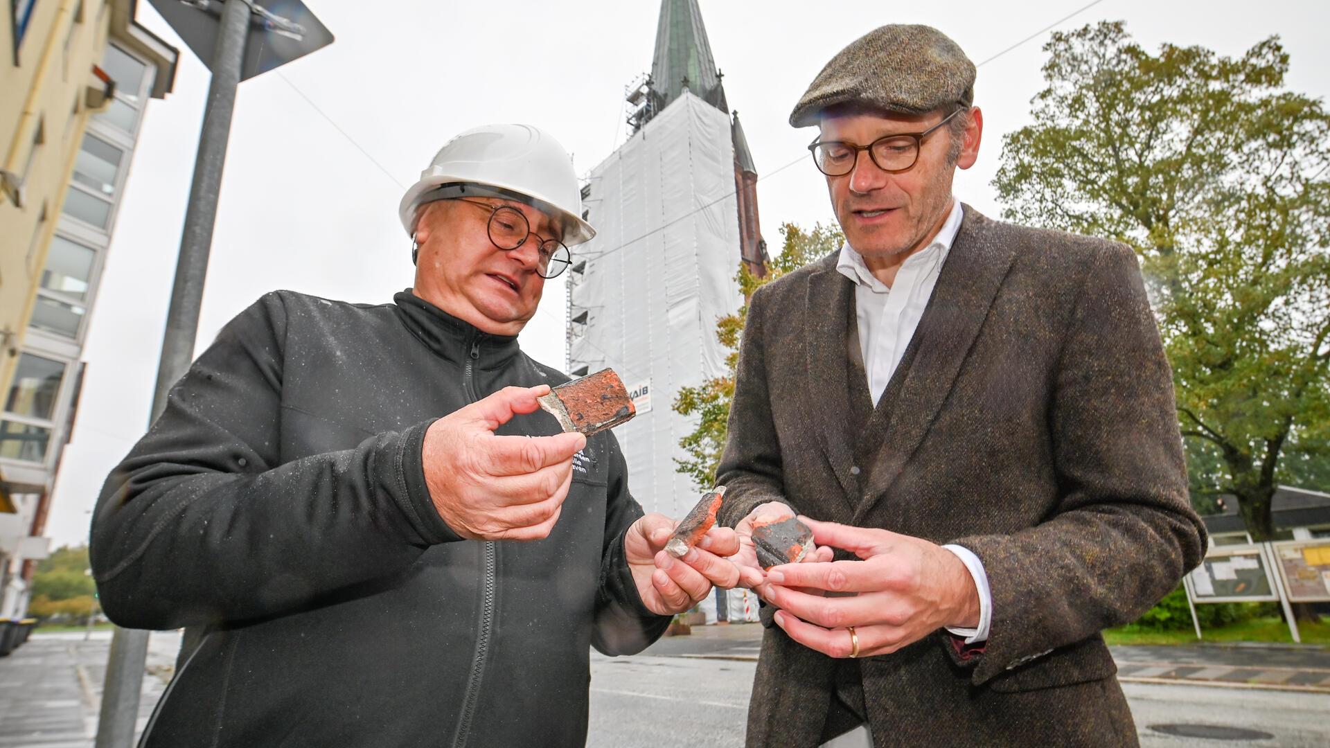 Solche Ziegelbröckchen fallen aus dem Mauerwerk des Turms der Geestemünder Christuskirche. Die Christus-und-Mariengemeinde musste kurzentschlossen reagieren, sagt Pastor Lars Christoph Langhorst (rechts) - und das Amt für Bau- und Kunstpflege der Landeskirche Hannovers alarmieren. Dessen Experte Dirk Tacke beaufsichtigt nun die Restaurierungsarbeiten.