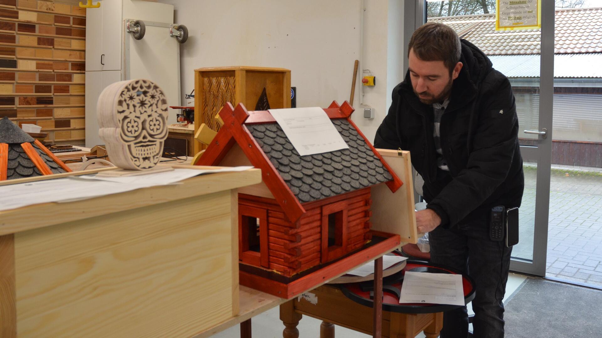 Ein Mann steht vor einem brauen Vogelhaus.