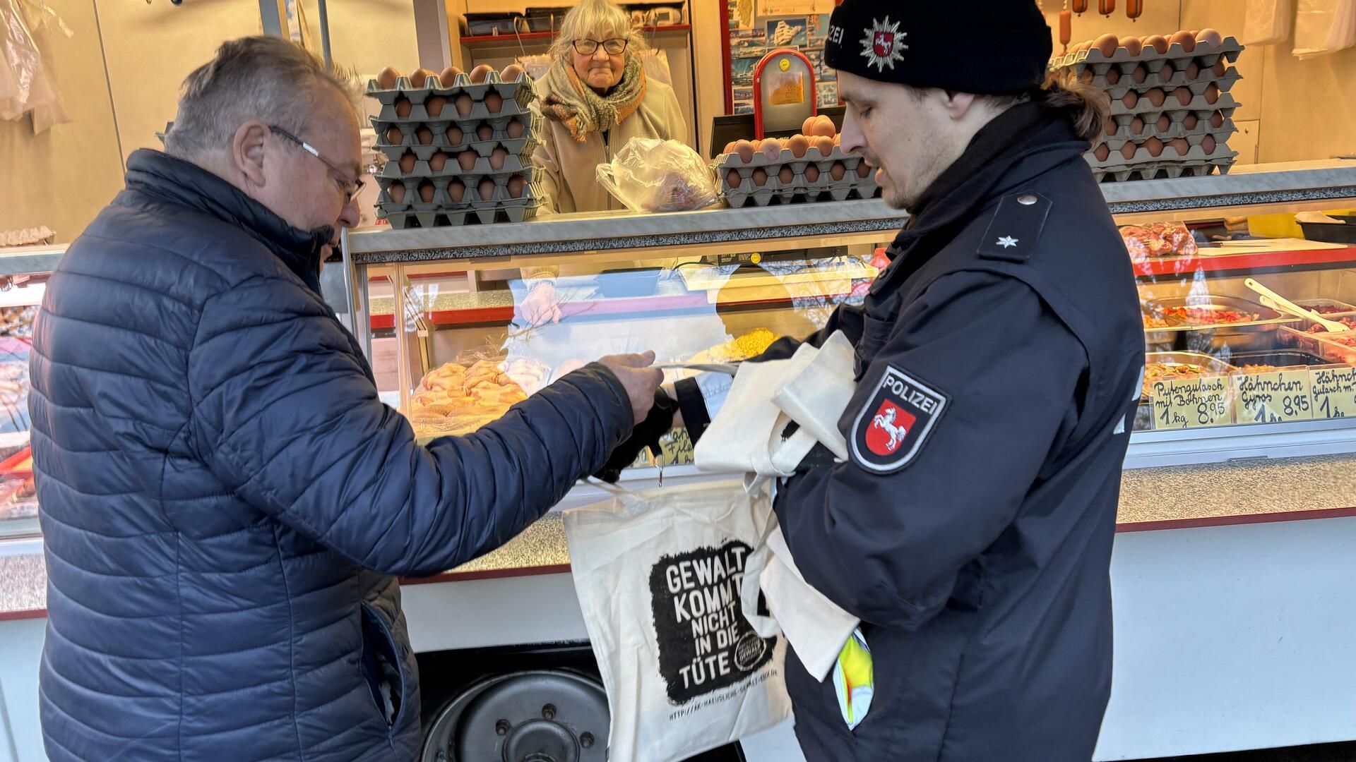 Kunde Günter Wilkens (links) nimmt aus den Händen von Polizeikommissar Fabian Ostrau eine Tasche entgegen. „Gewalt kommt nicht in die Tüte“ steht darauf.