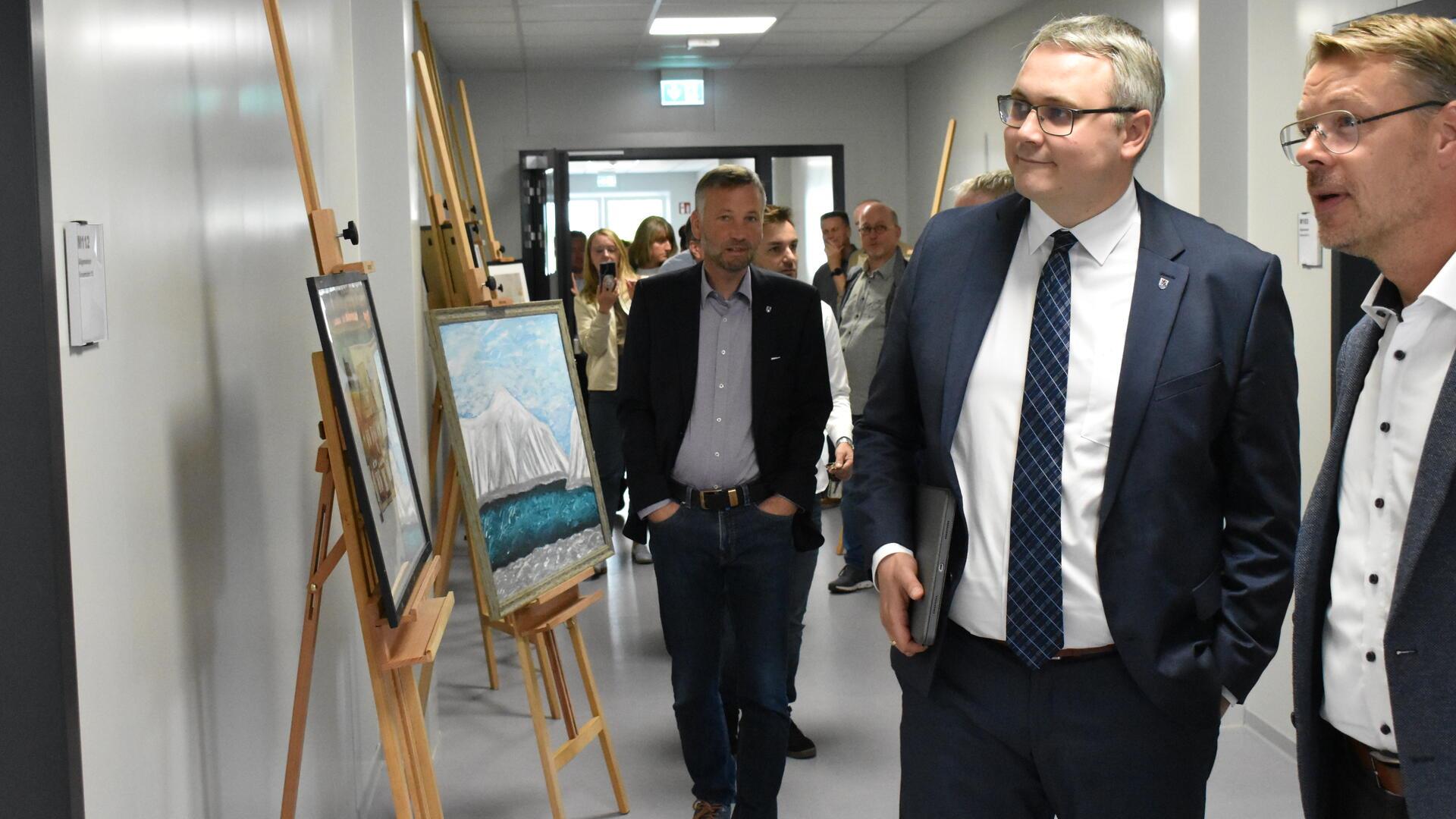 Zwei Männer in Anzügen stehen rechts im Bild, links stehen Staffeleien mit Bildern.