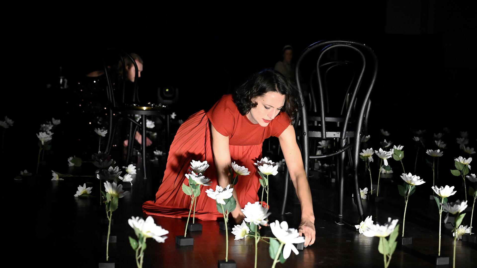 Schauspielerin in einem roten Kleid und Blumen auf einer Bühne, kniend