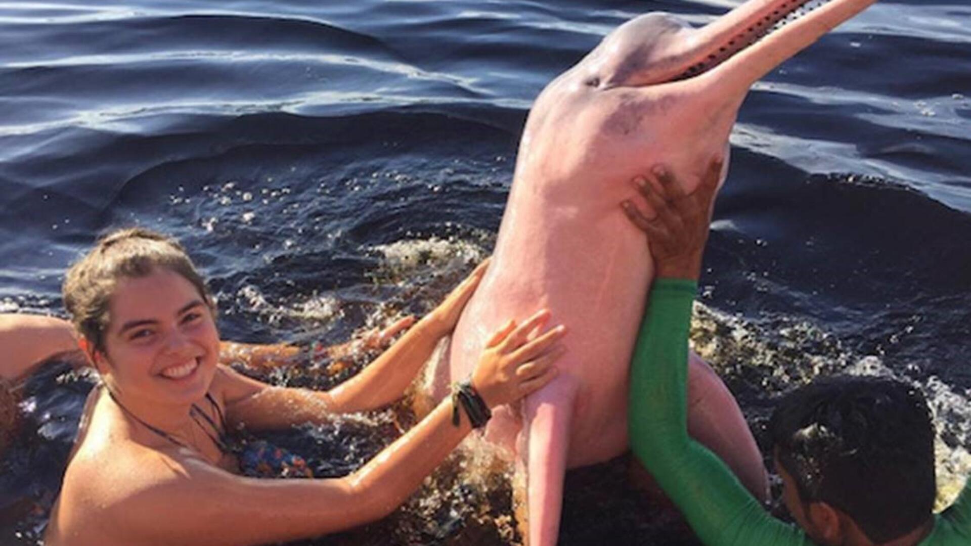 Das Foto zeigt Laura Gawehn, wie sie im Meer einen rosa Delfin streichelt. 