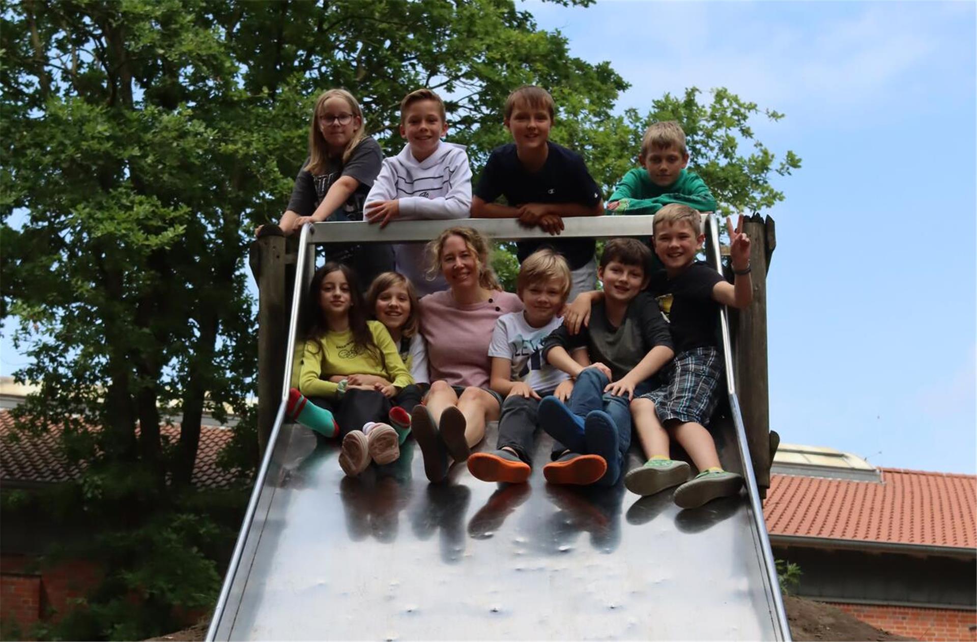 Kinder sitzen mit ihrer Lehrerin auf einer Rutsche.