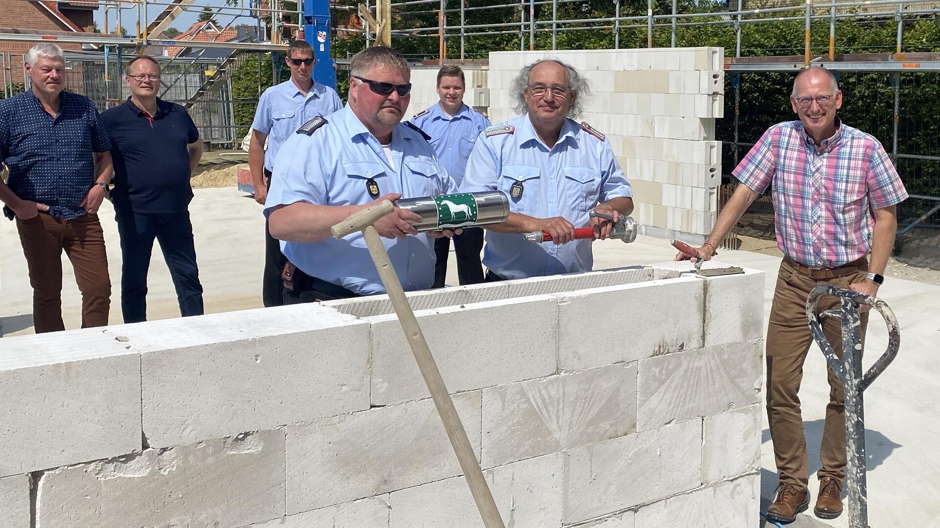 Sieben Männer stehen an einer hüfthohen Mauer und platzieren eine silberne Zeitkapsel sowie ein Stahlrohr im Mauerwerk