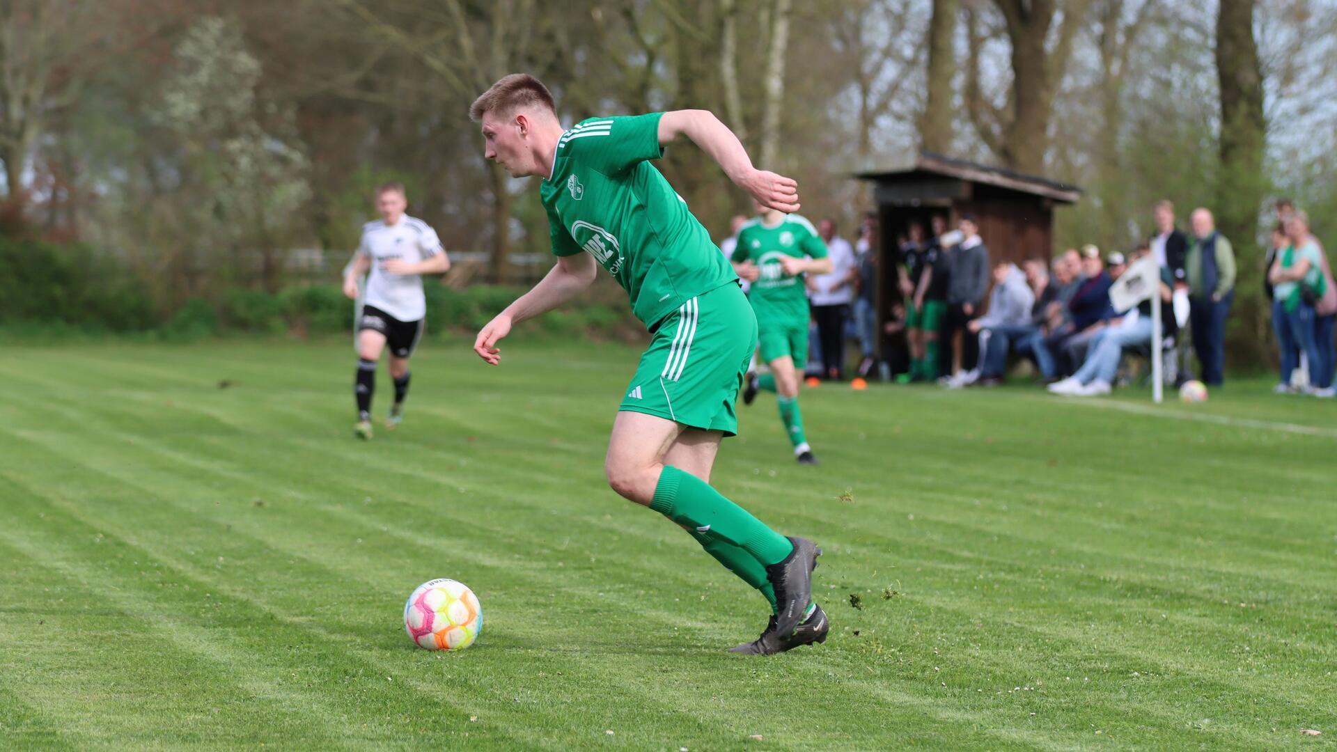 Ein Mann in einem grünen Trikot läuft hinter einem Ball her.