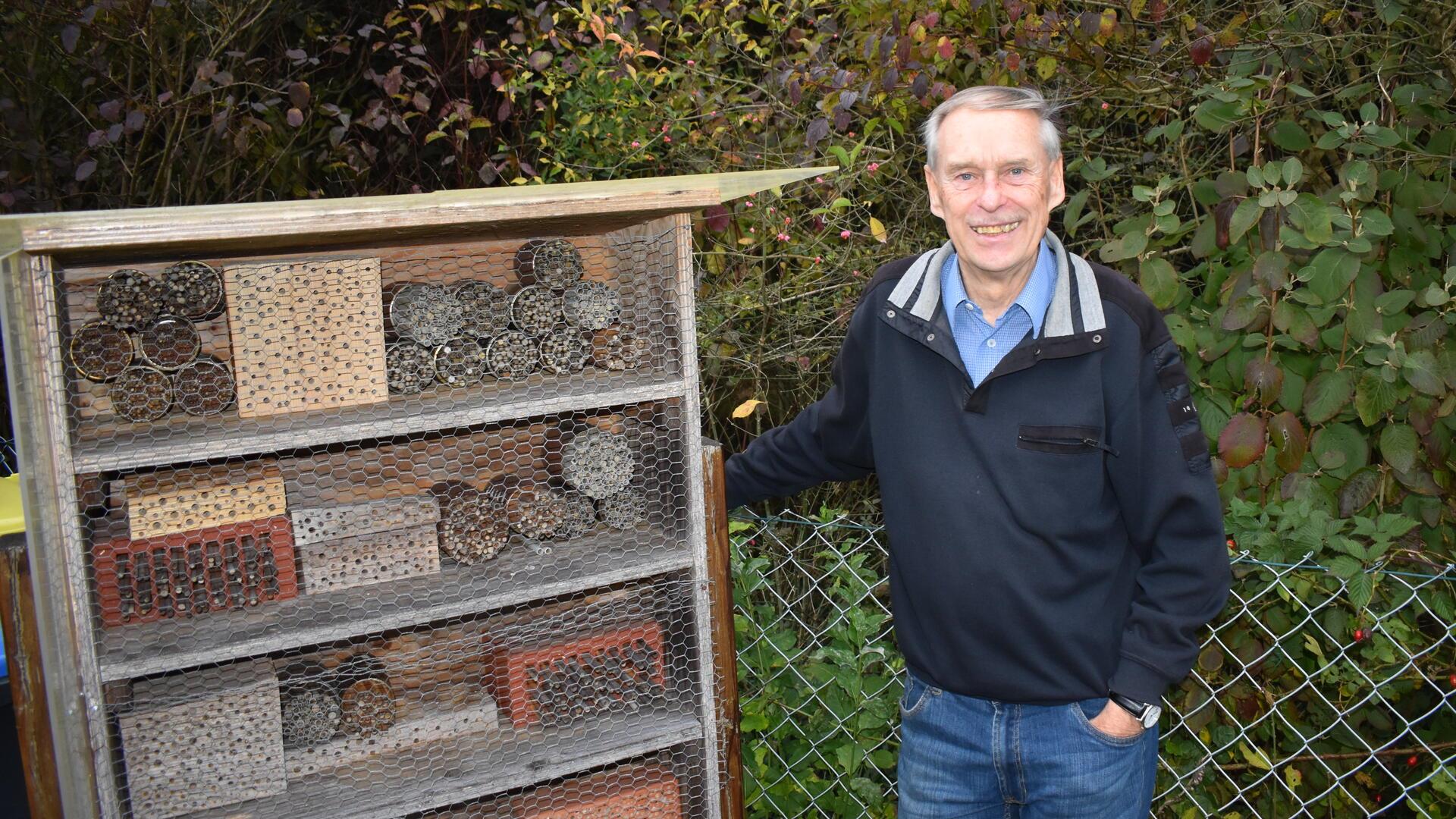 Ein älterer Mann steht neben einem Stand mit Insektennisthilfen.