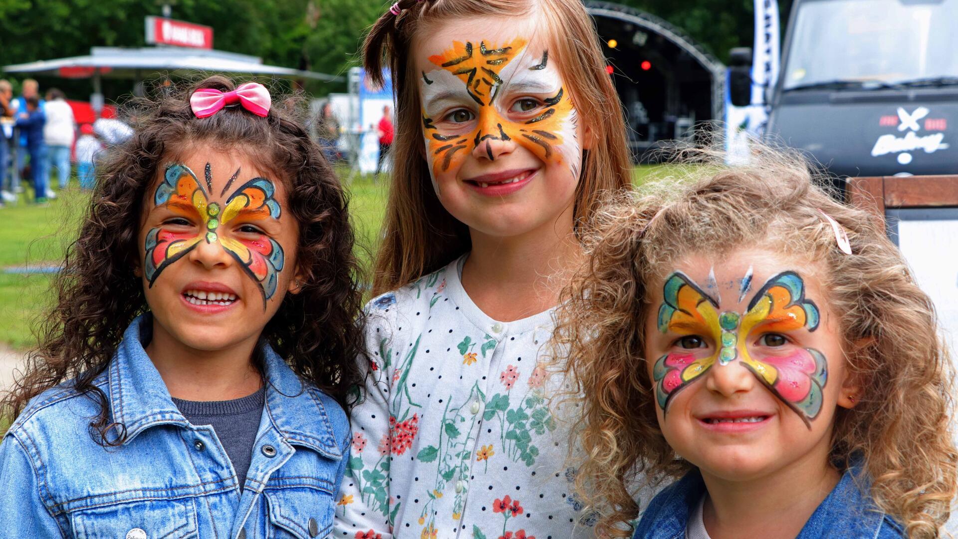 Drei kleine Mädchen, die in bunten Farben bemalte Gesichter haben.