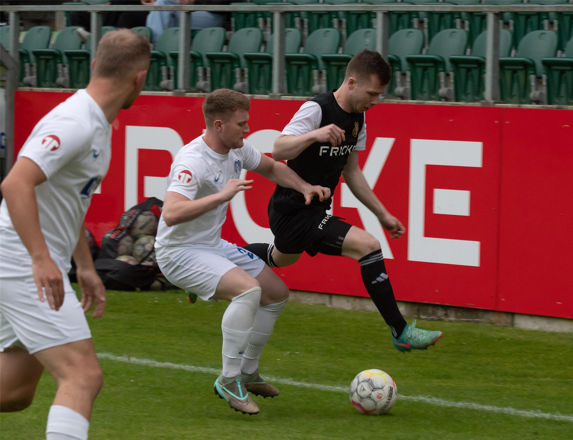 ein Mann in einem schwarzen Trikot und zwei Männer in einem weißen Trikot mit einem Fußball