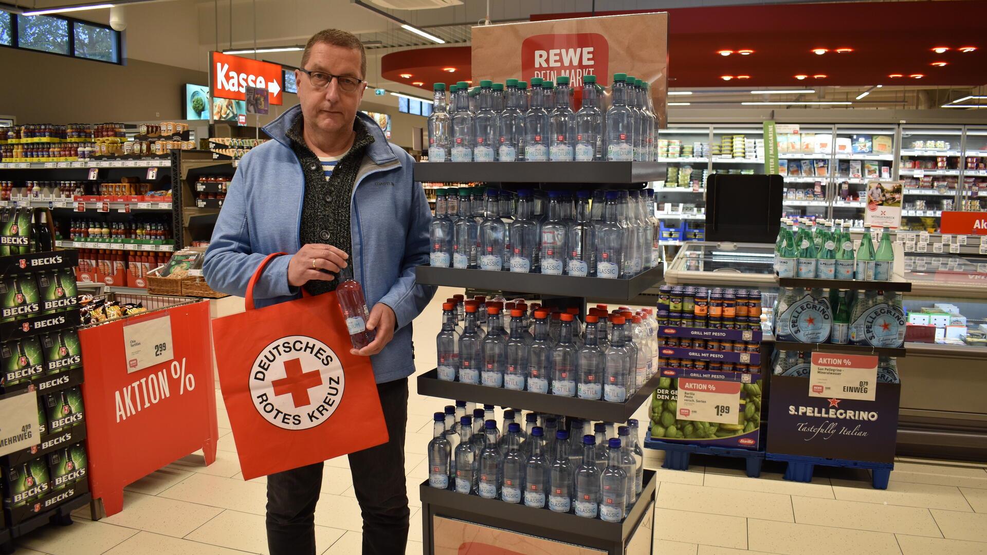 Michael Lewin steht an einem Aufsteller im Supermarkt (Rewe, Nordholz) mit Wasserflaschen.