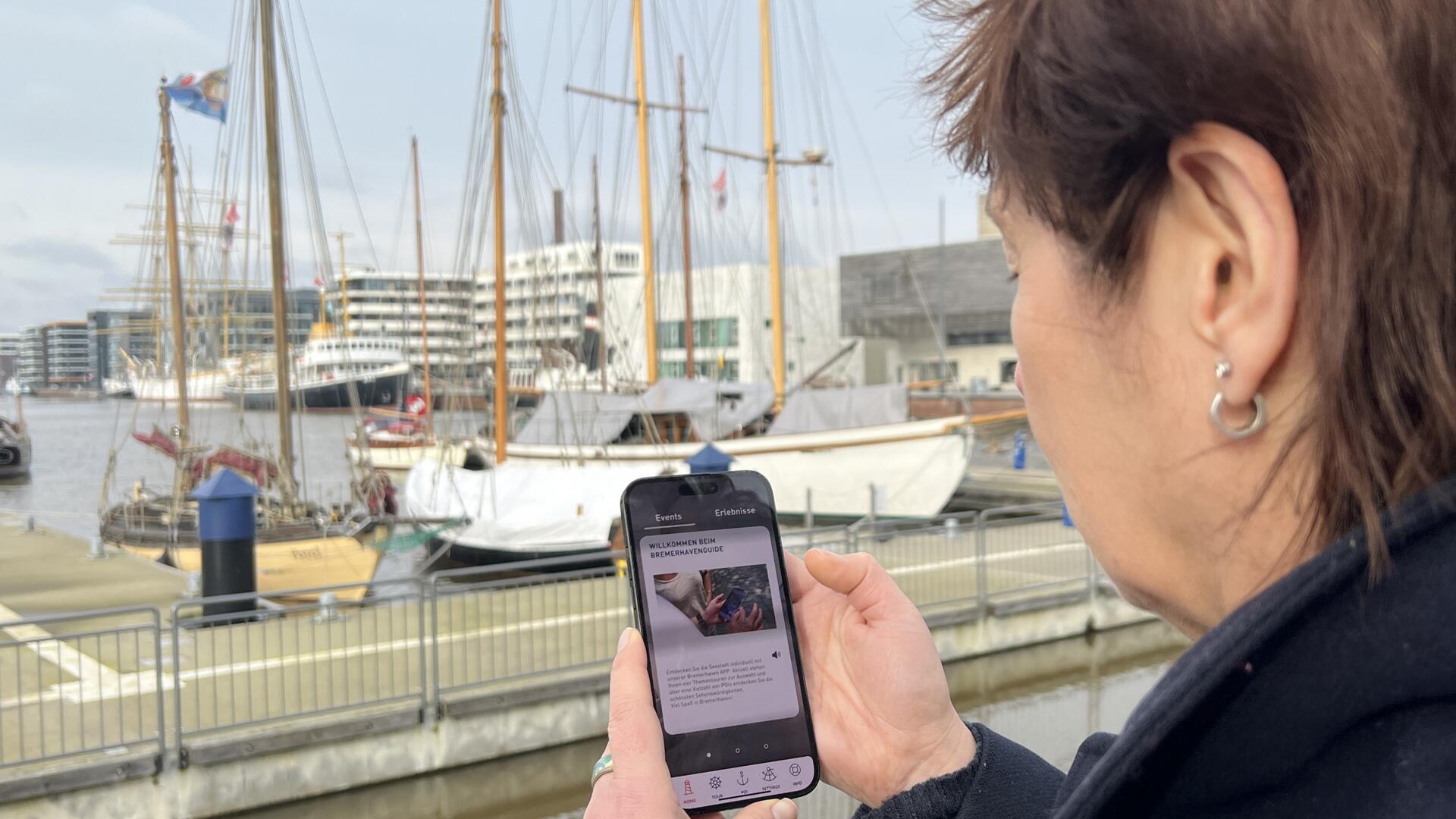 Eine Frau steht im Hafengebiet und schaut auf das Display ihres Smartphones.