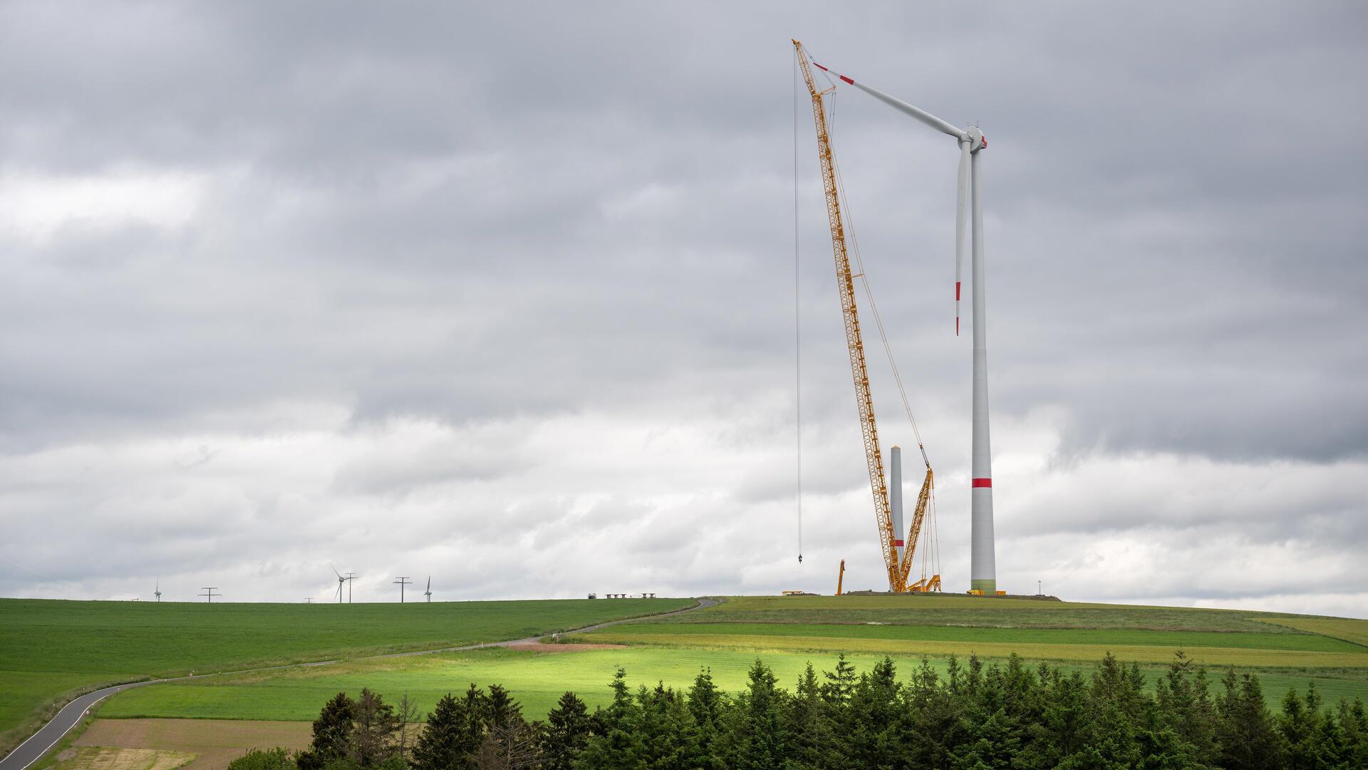 Während dichte, dunkle Wolken am Himmel ziehen, werden im Windpark Obergeckler riesige Windkraftanlagen errichtet.