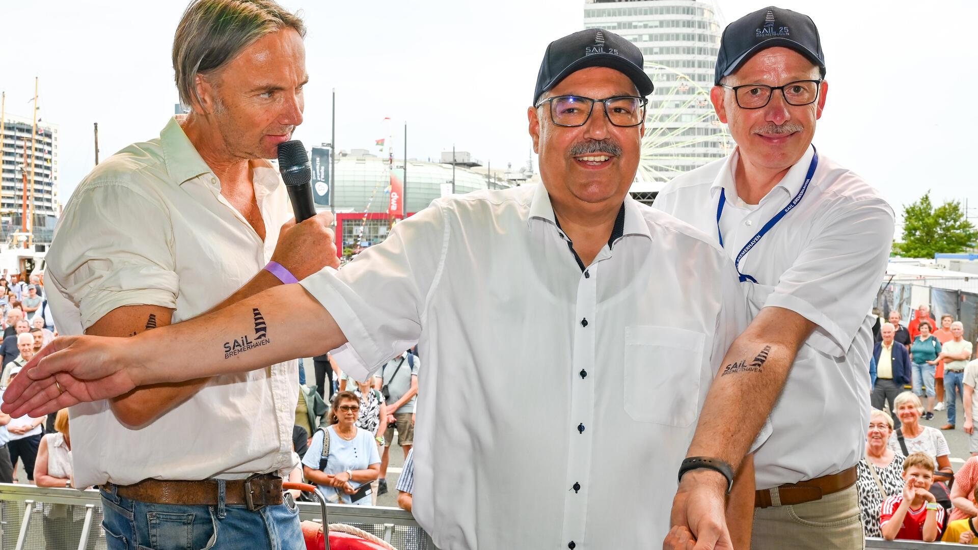 Mit über 60 zum ersten Tattoo: Bei der Eröffnung der Maritimen Tage erhielten Oberbürgermeister Melf Grantz (Mitte) und Stadtverordnetenvorsteher Torsten von Haaren (rechts) ein Klebe-Tattoo mit dem Sail-Schriftzug und Segeln. Ansgar Langhorst von Radio Bremen moderierte das Ganze.