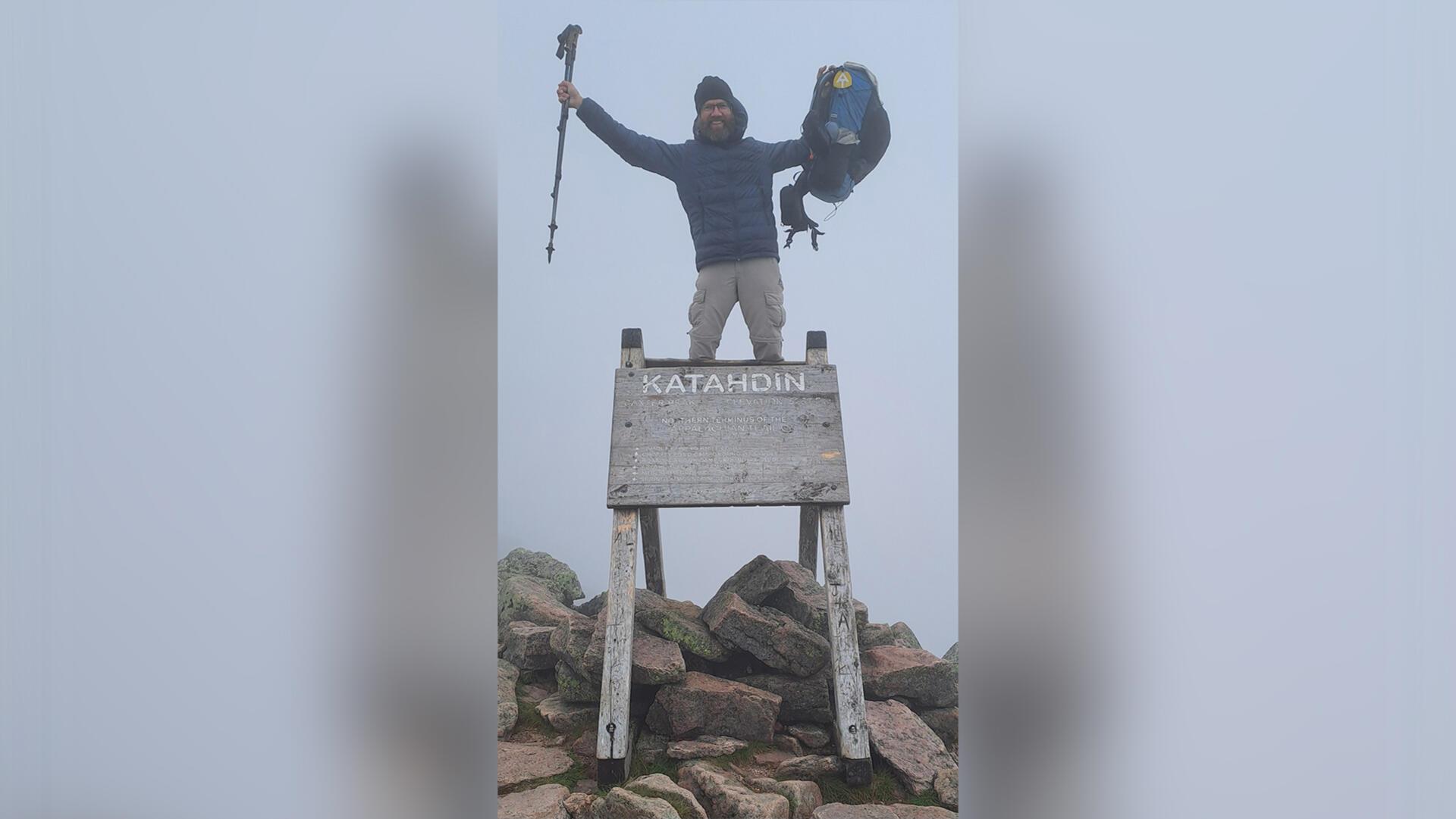 Ein Mann posiert mit Rucksack und Wanderstöcken auf dem Gipfel des Mount Katahdin.