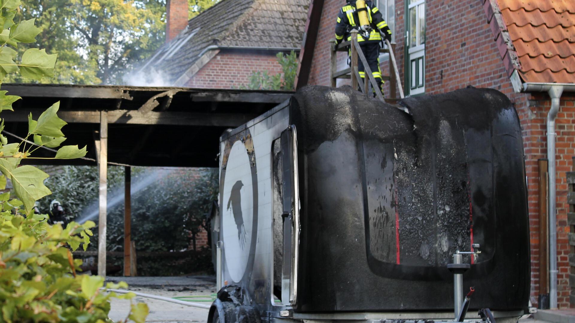 Nachlöscharbeiten an einem Carport, im Vordergrund ein verbrannter Pferdeanhänger.