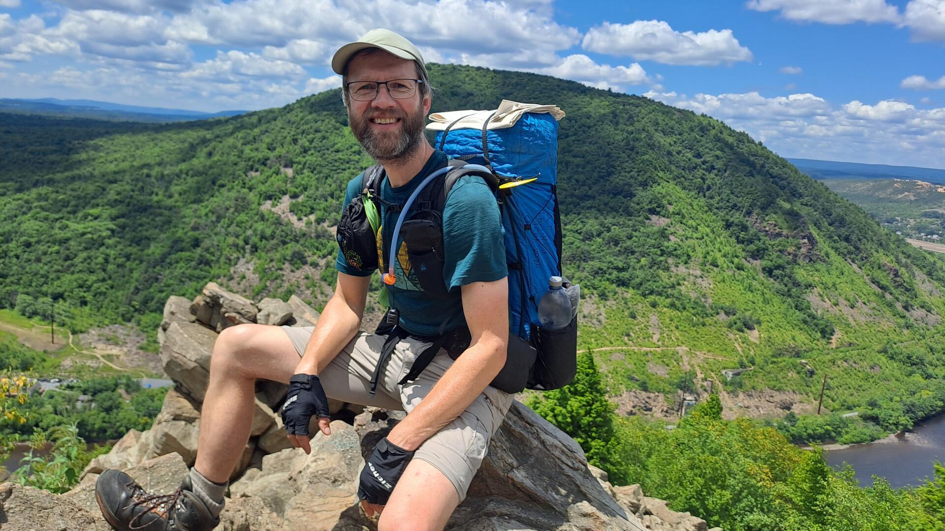 Ein Mann sitzt auf einem Felsen und blickt in die Kamera.