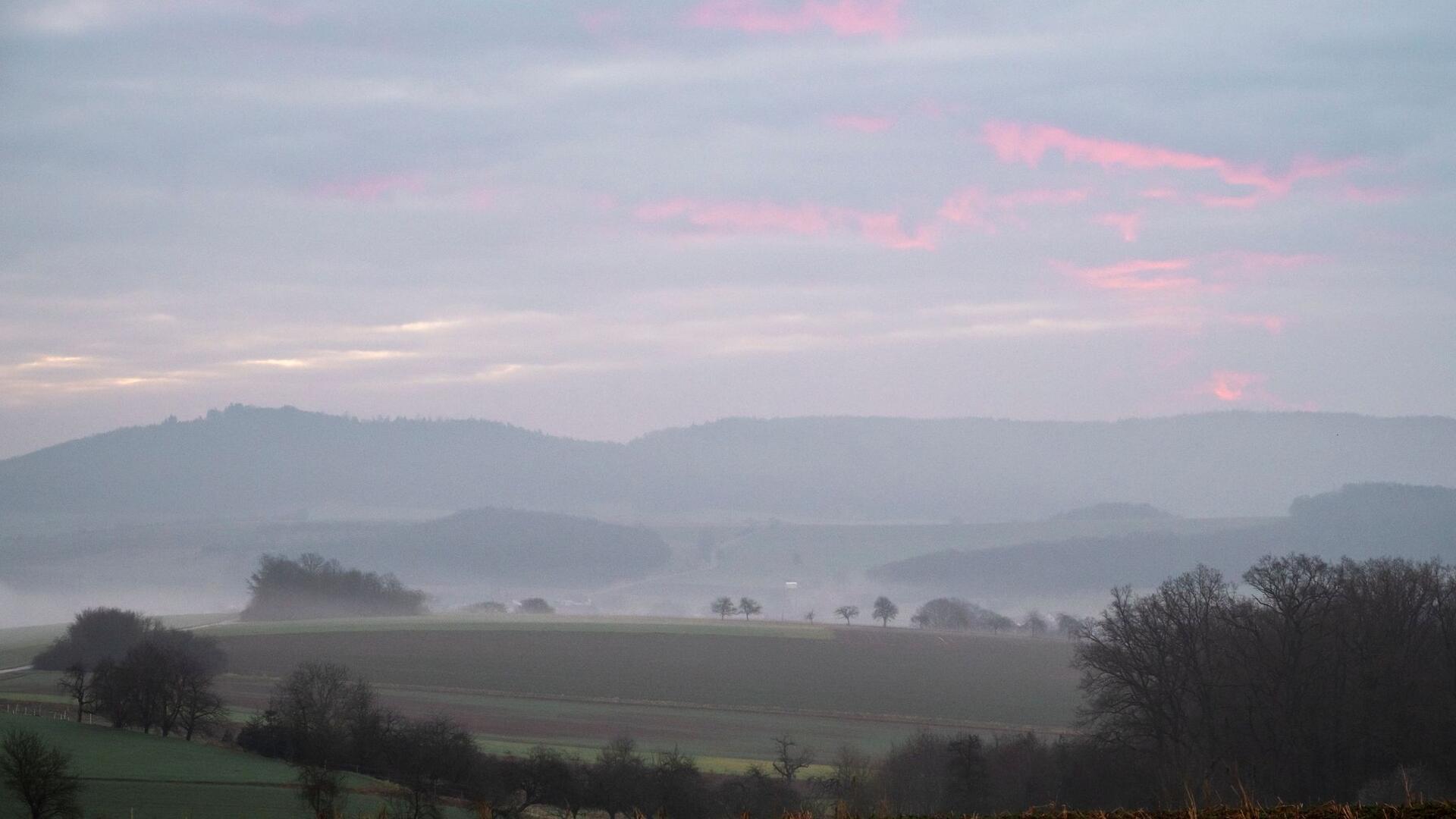 Neblige bayerische Landschaft mit Morgenrot am Himmel.