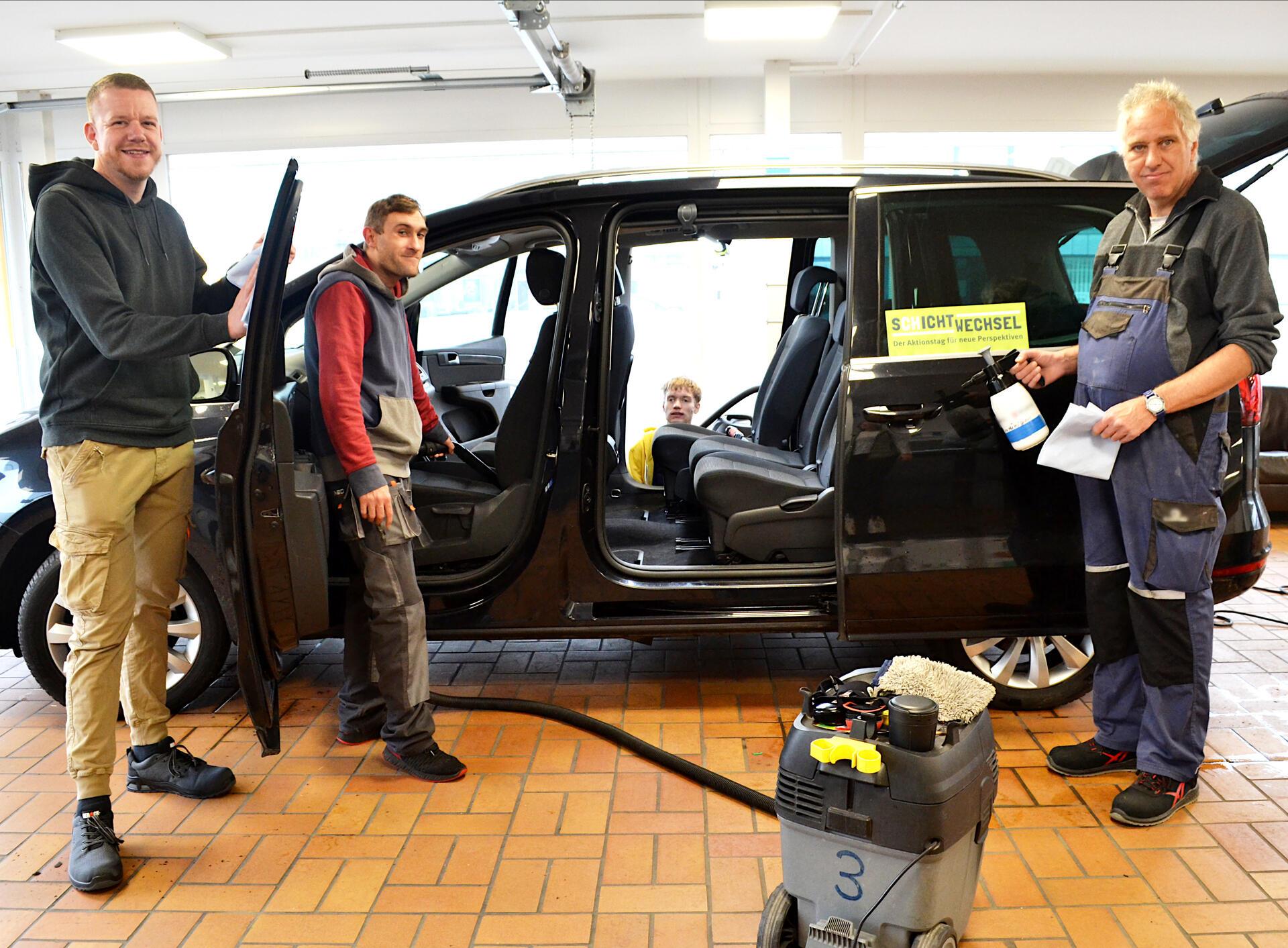 Drei Männer in einer Auto-Werkstatt. 