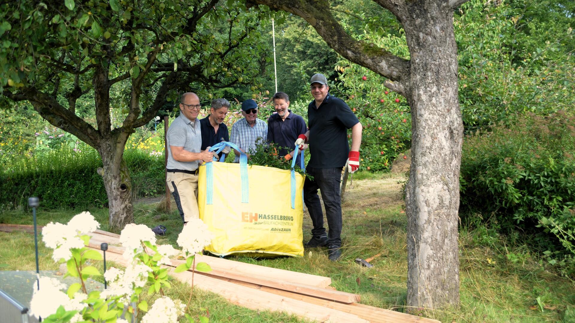 Fünf Männer stehen im Garten und halten zusammen einen Sack in der Hand.