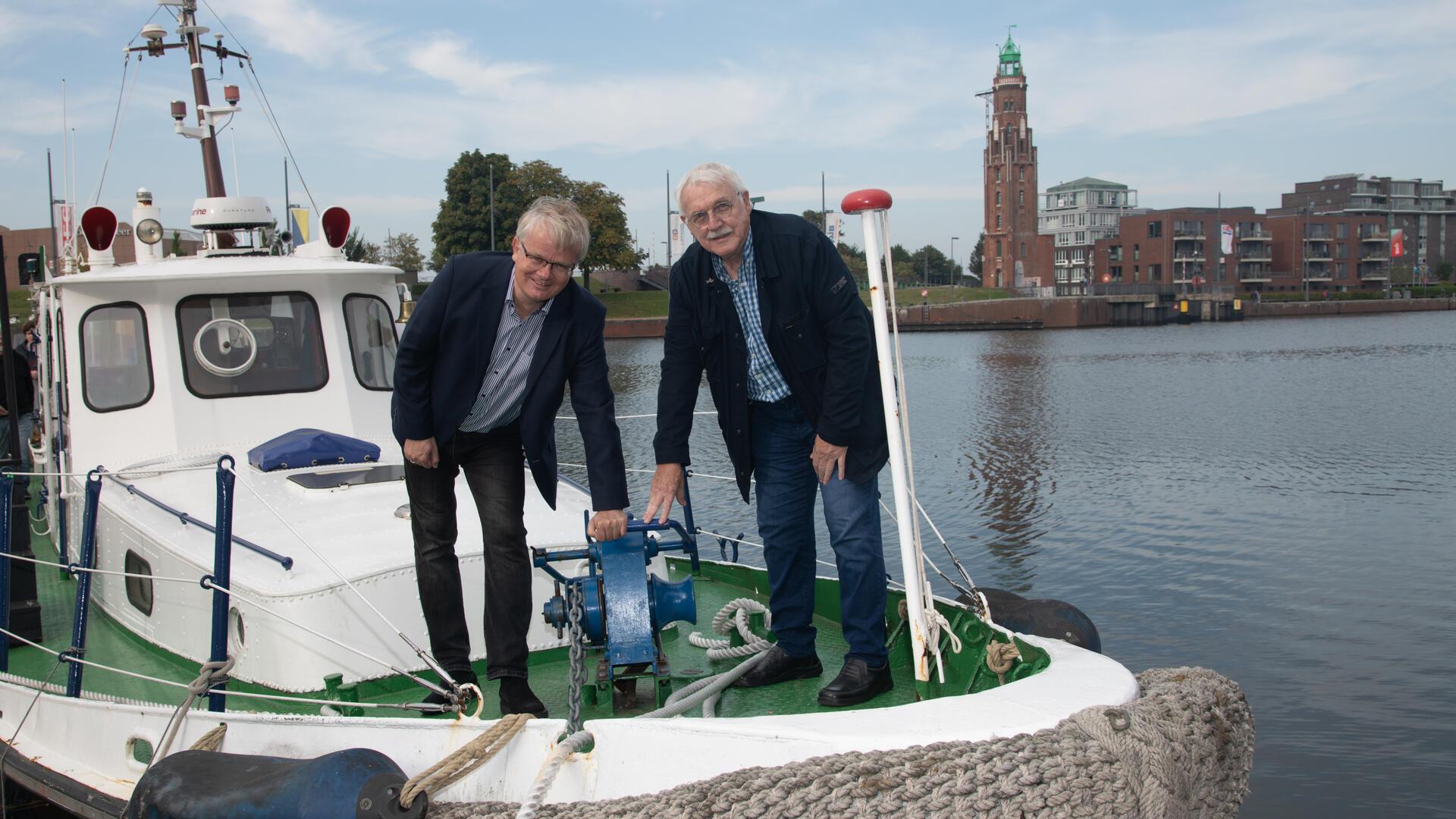 Peter Klett (Stiftung Maritimes Erbe) und Reiner Schumacher (Stammtisch Unterweser) an der Winsch des historischen Schiffs „Quarantäne“ als symbolisches Zeichen der Verbundenheit bei der Spendenübergabe.