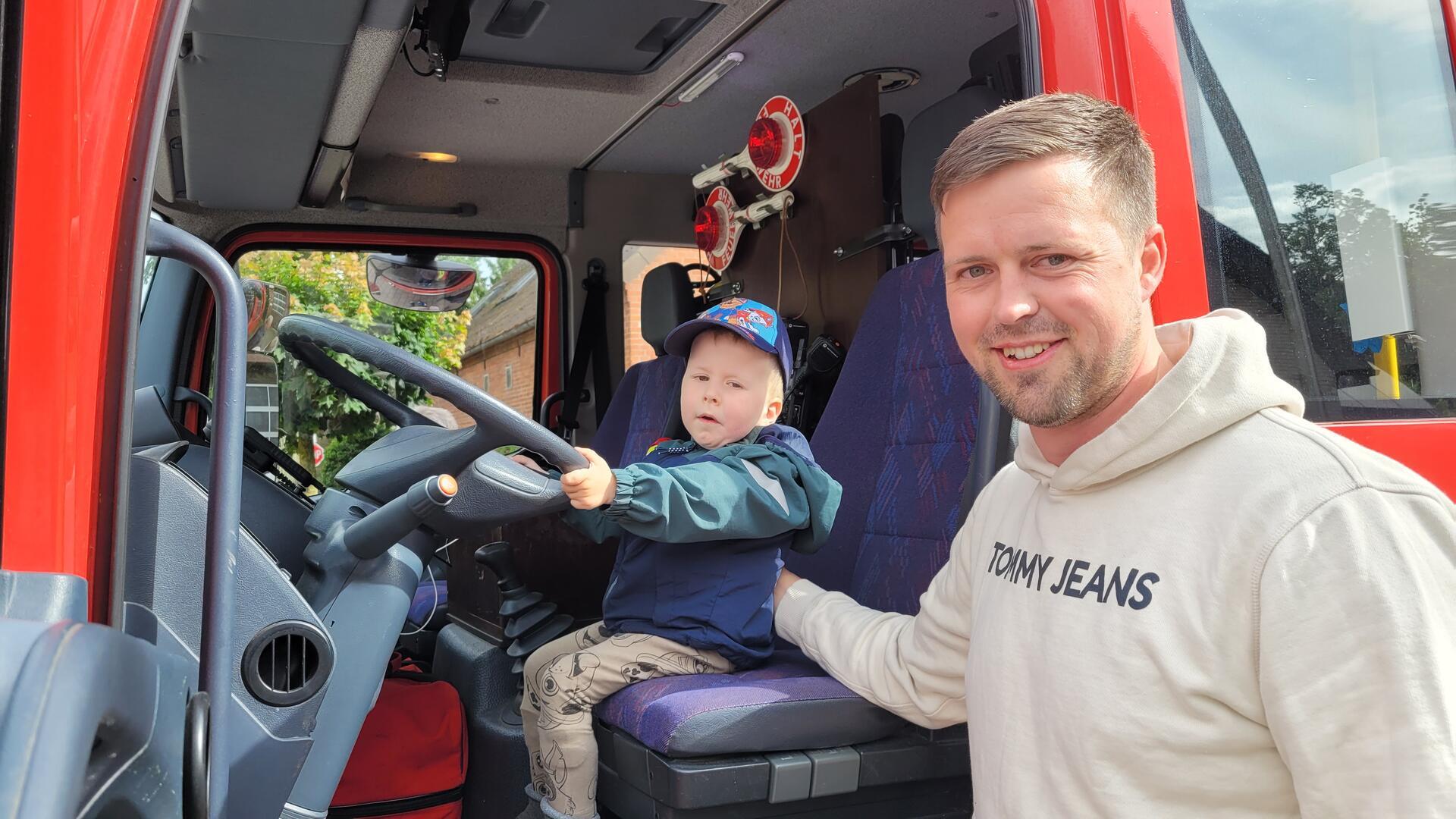 Probesitzen bei der Wremer Feuerwehr: Während sich Papa Marcel Bursky über eine großzügige Spende freut, blüht Söhnchen Theo auf dem Fahrersitz des Feuerwehreinsatzwagens auf.