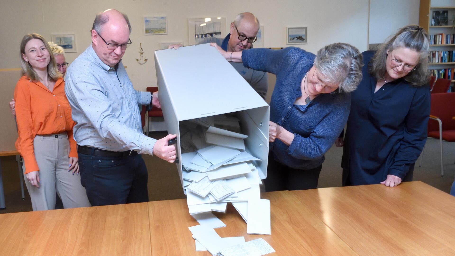 Zwei Personen leeren den Inhalt einer Wahlurne auf einen Tisch. 