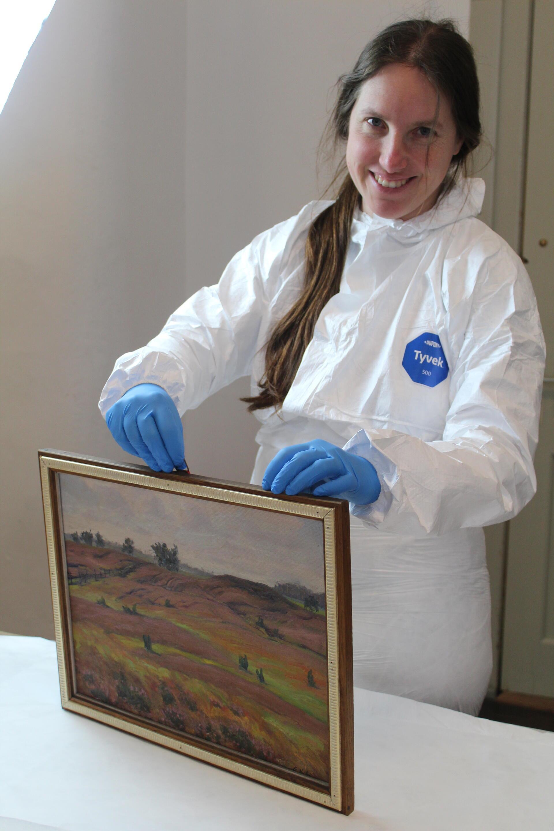 Restauratorin Jasmin Wollenhaupt bei der Begutachtung des Gemäldes „Hügelgrab Nr. 18 auf dem Langenberg bei Sassenholz“ von Emil Schache.