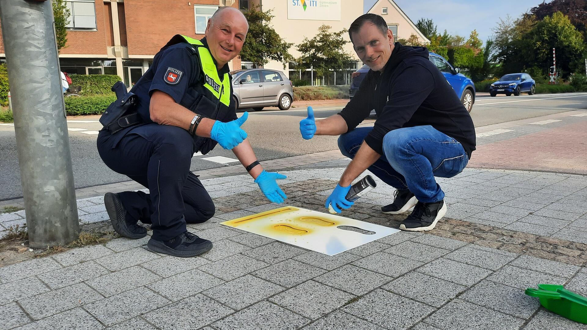 Rolf Meyer und Kristian Kugeler sprühen mit gelber Farbe Füße auf den Gehweg. 