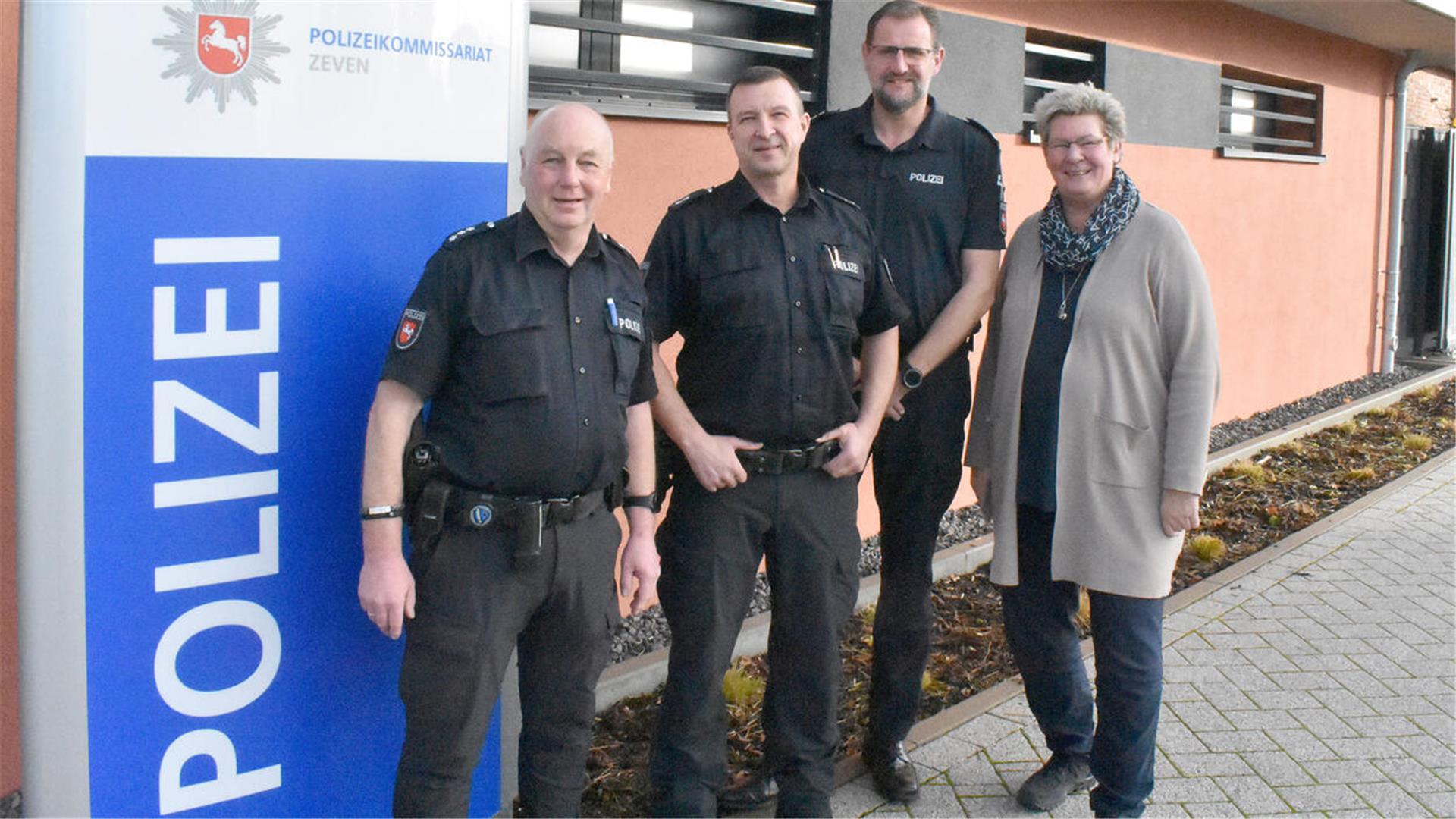 Drei Männer und eine Frau stehen neben einem großen Schild, auf dem Polizei steht.