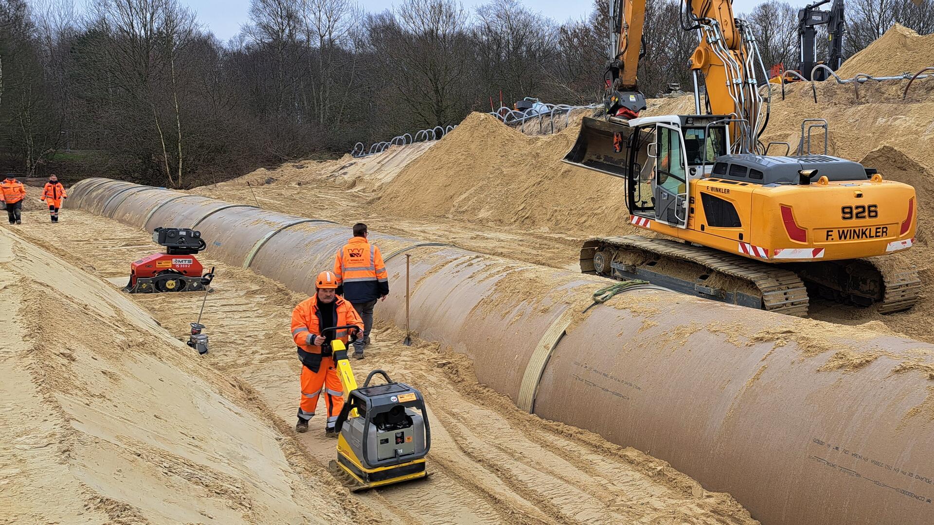 Schicht für Schicht verdichten die Bauarbeiter den Sand mit Rüttelplatten, damit das neue Rohr fest sitzt. 