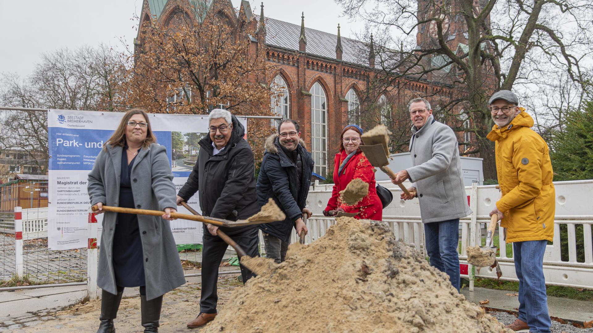 Vier Männer und zwei Frauen haben Spaten in der Hand und schippen Sand.