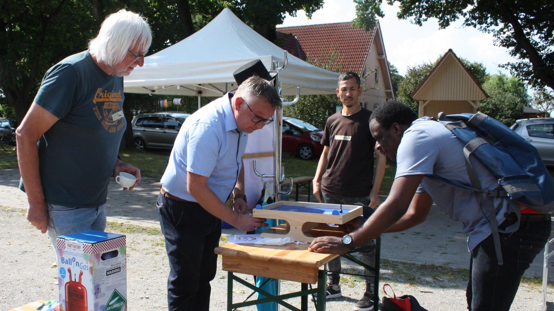 Vier Männer stehen rund um einen Klapptisch, auf dem zwei der Männer eine Partie Magnetfußball spielen.