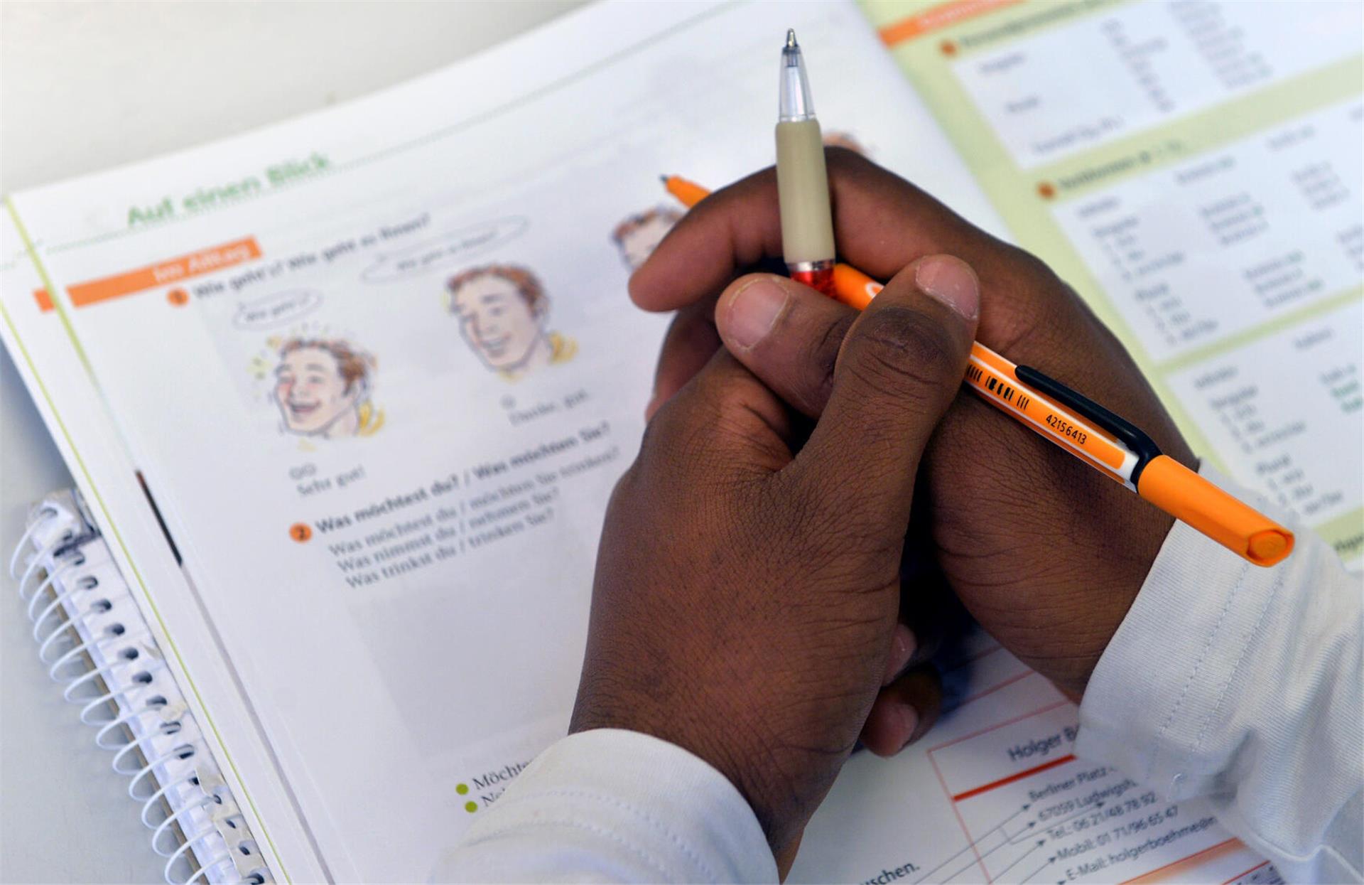  Ein Lehrbuch liegt in einem Deutschkurs für Flüchtlinge vor einem jungen Mann auf der Schulbank. 