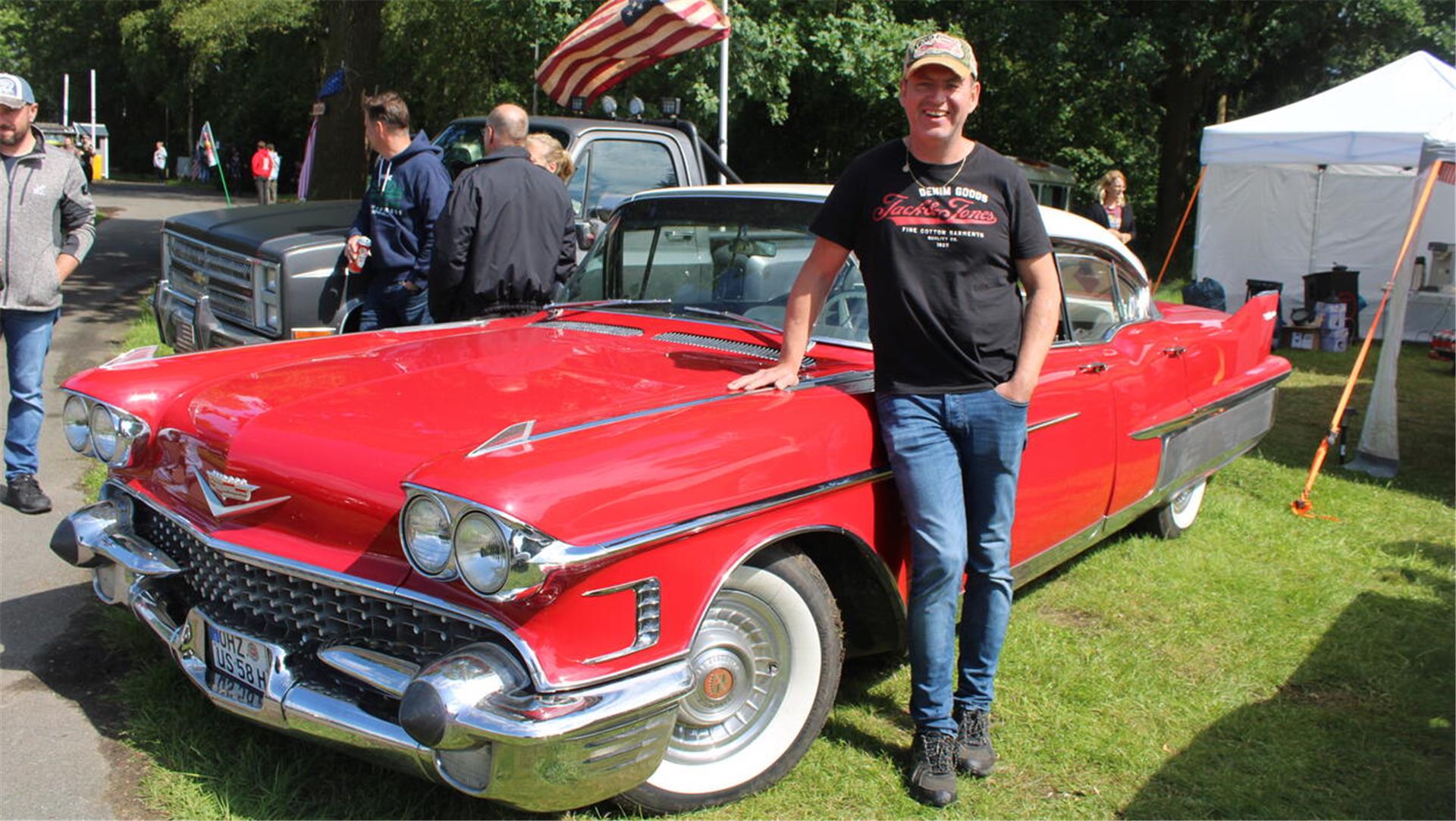 Ein Mann in Jeans und T-Shirt lehnt an seinem roten US-Oldtimer der Marke Cadillac