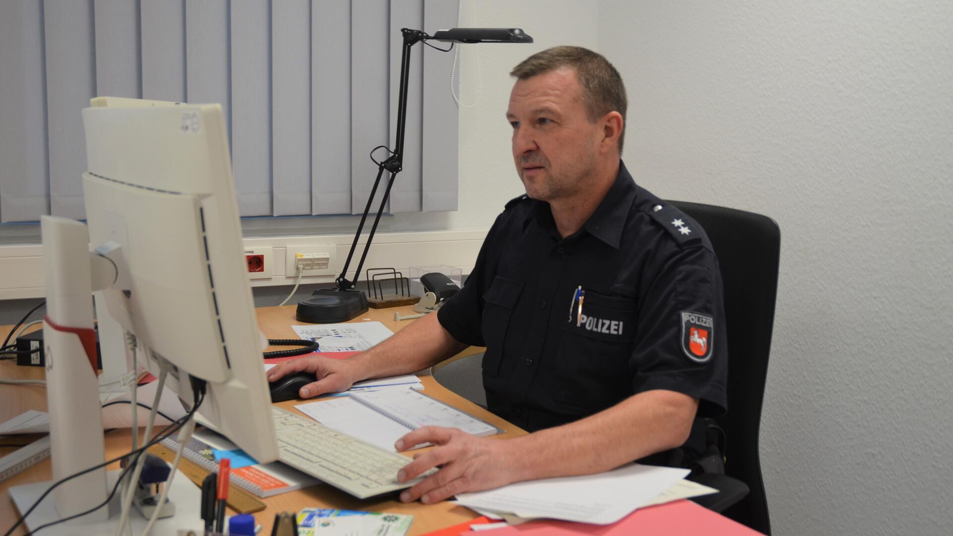 Ein Mann in Polizeiuniform mit kurzen dunklen Haaren sitzt vor einem Computer und schaut auf den Bildschirm. 