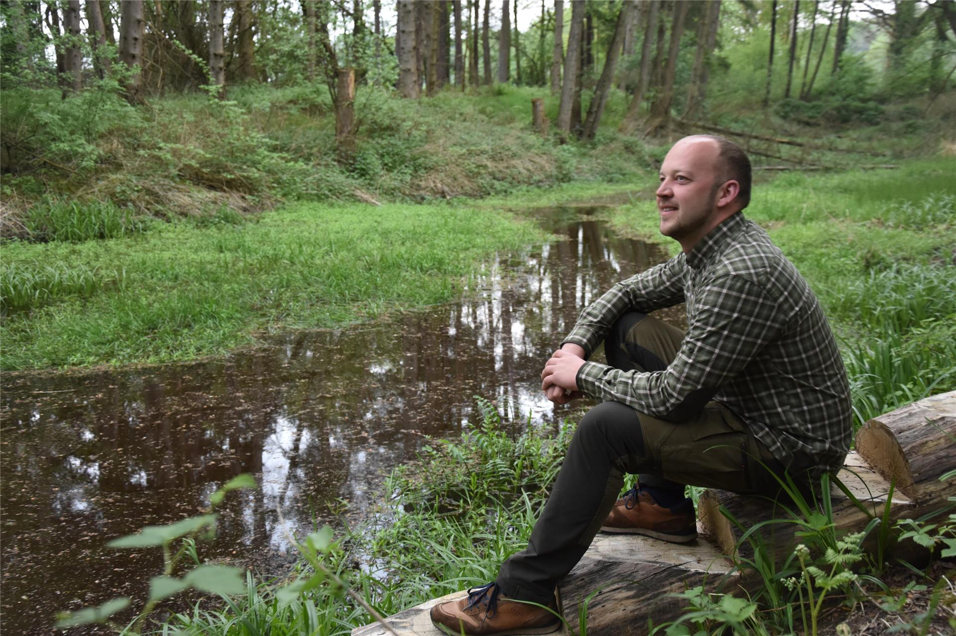 Das Foto zeigt Thorben Rievesehl an einem Teich im Wald sitzend.  