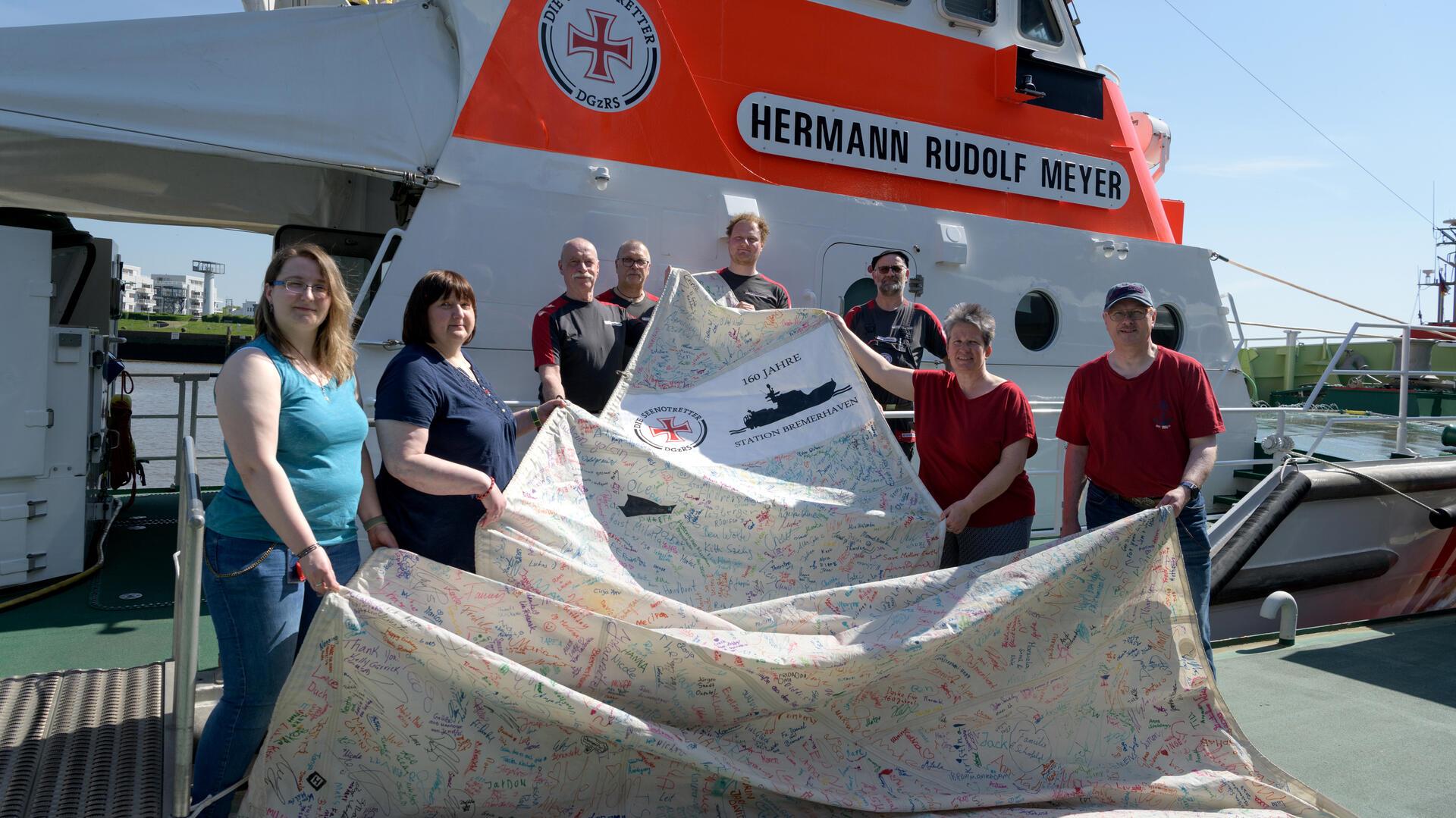 Tolle Aktion der Ehrenamtlichen: Zusammen mit den Bremerhavener Seenotrettern zeigen sie eins von vier signierten Segeln.