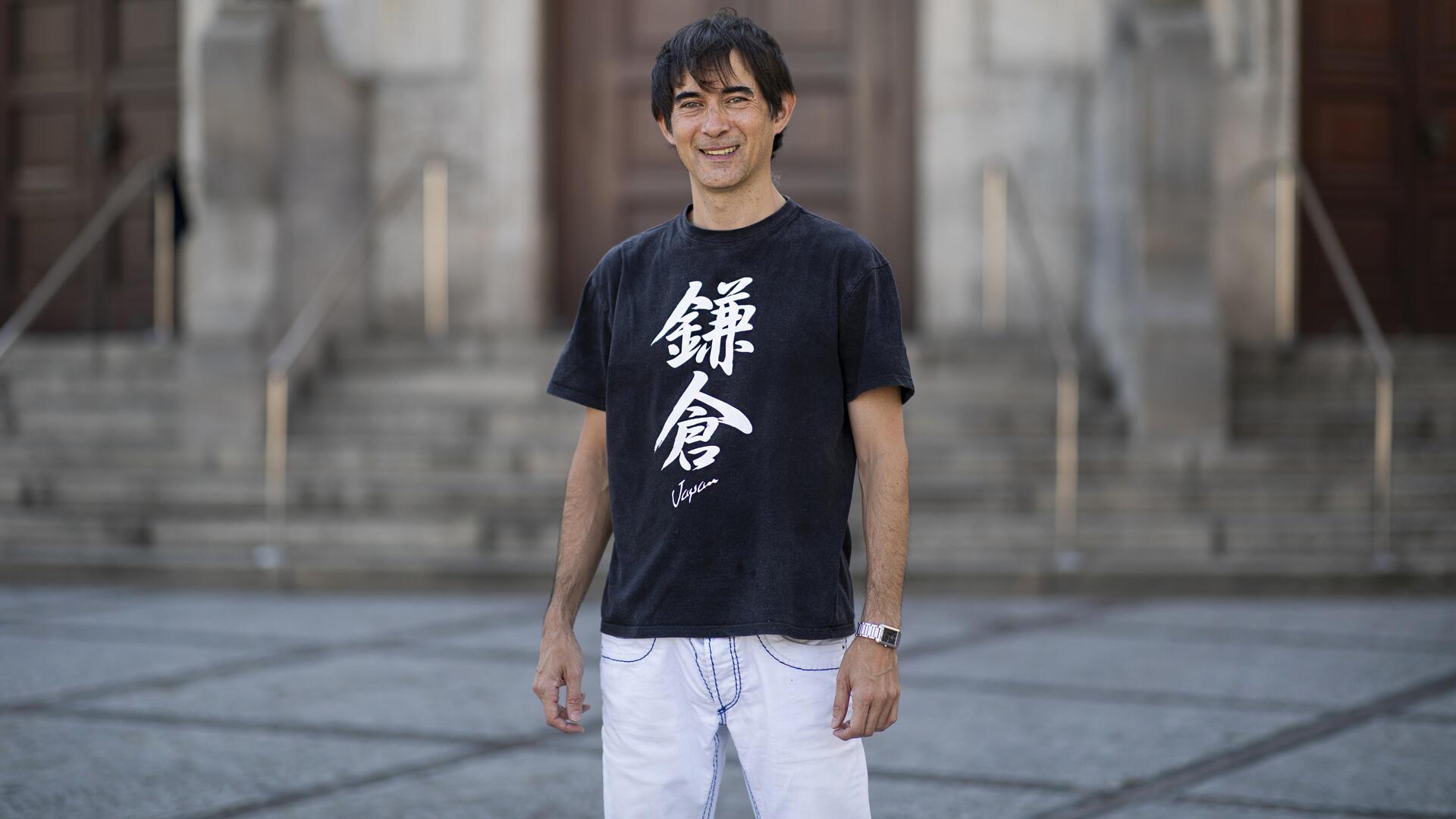 Ein Mann trägt ein schwarzes T-Shirt mit japanischen Schriftzeichen und eine weiße Hose.