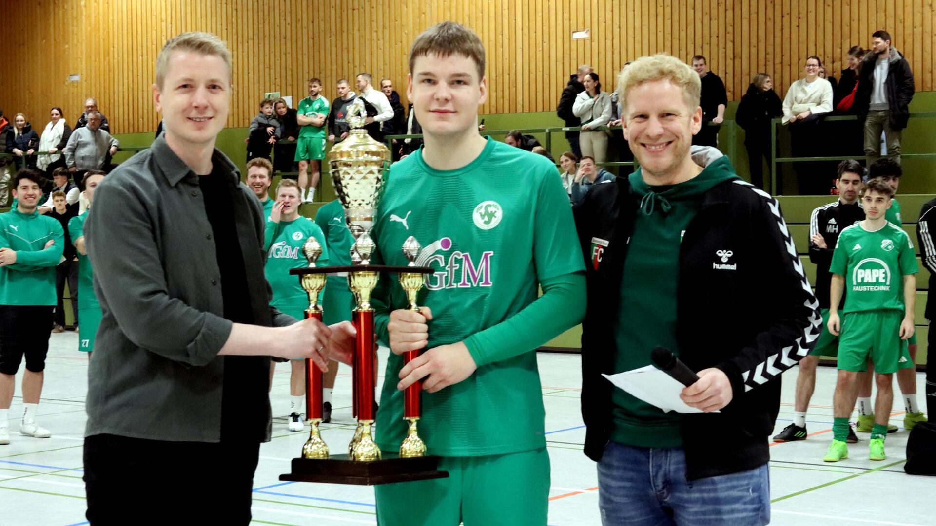 Turniersponsor Marvin Pape (l.) und Lukas Ringen überreichen VSK-Kapitän Tjerk Johannsen den Siegerpokal.