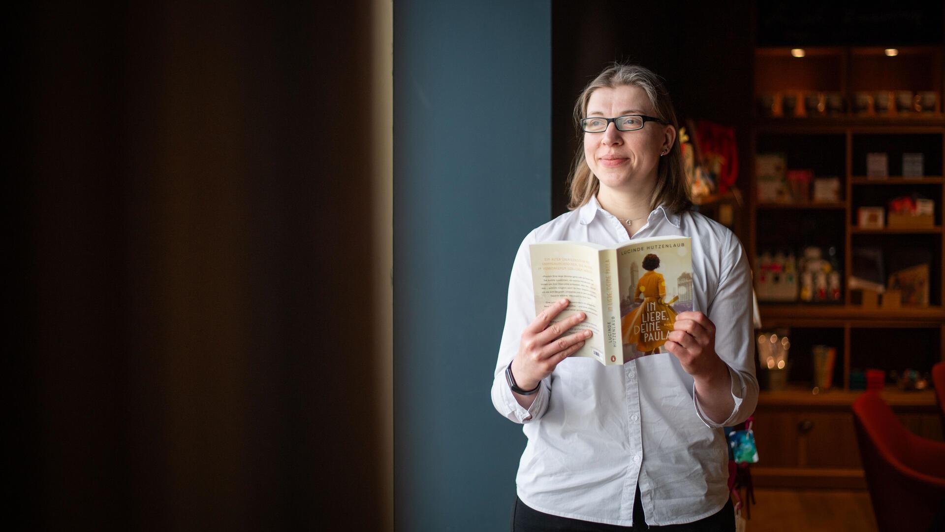 Eine Frau mit weißer Bluse trägt hält ein Buch in der Hand.