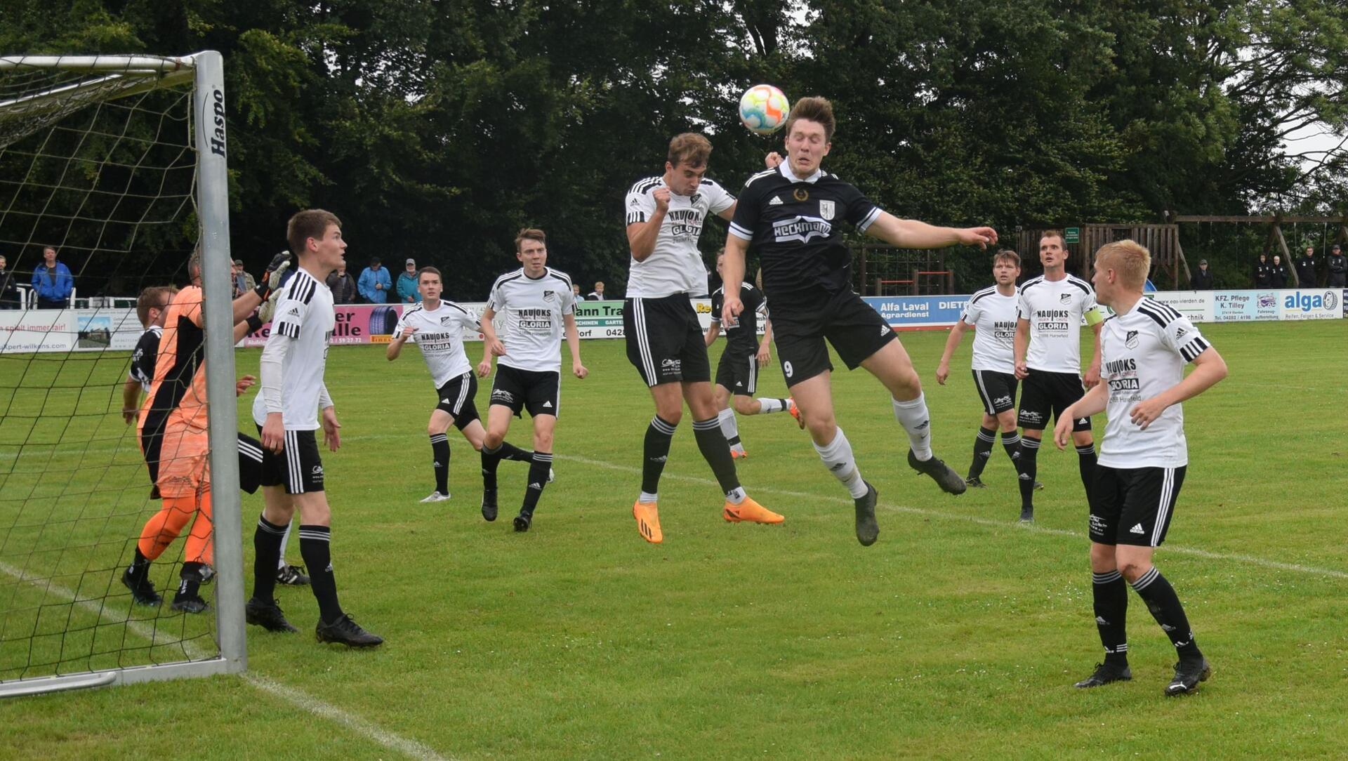 Zwei Männer springen zu einem Ball hoch und sechs Männer schauen zu.