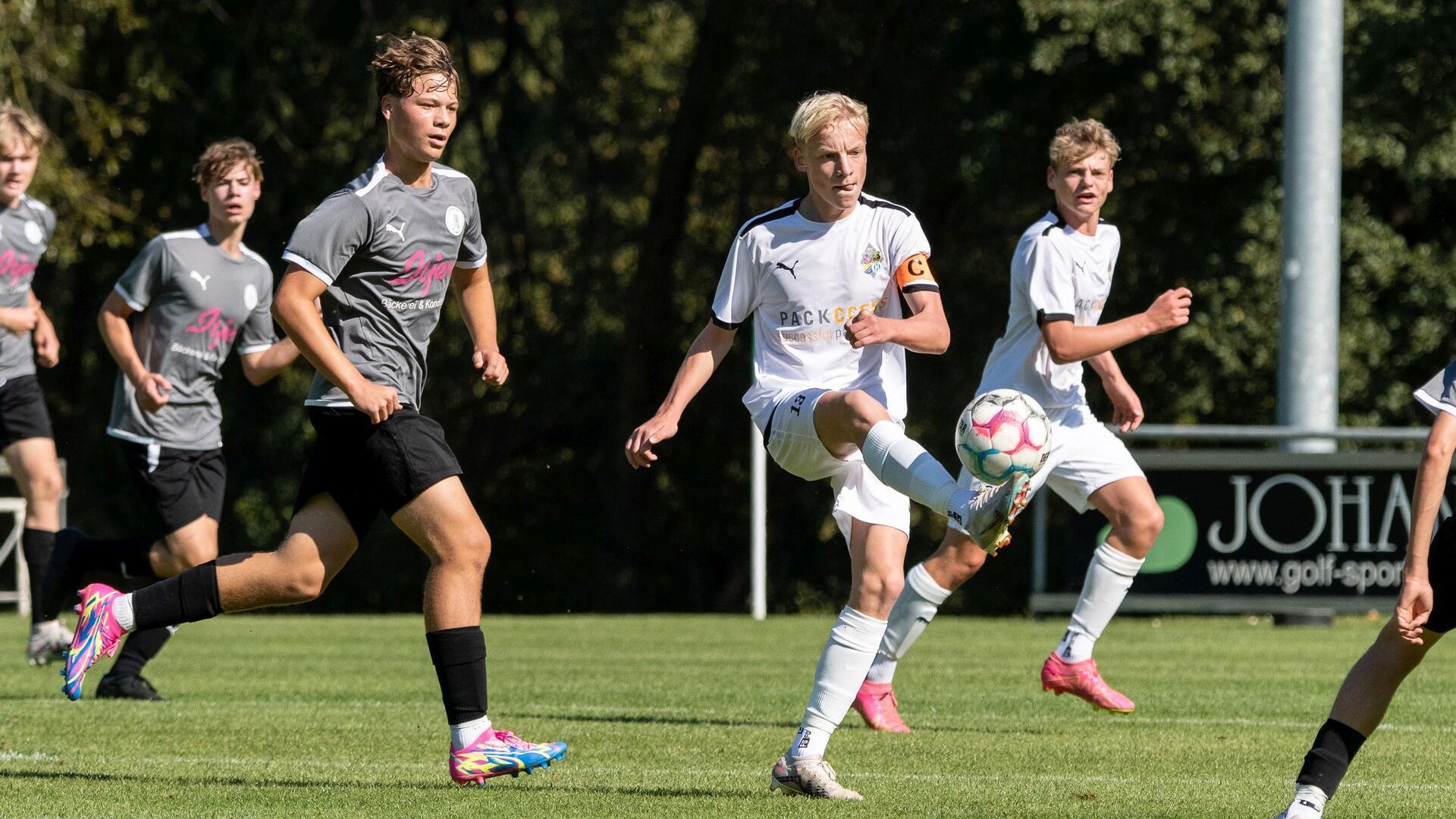 Zwei junge Männer in weißen Trikots laufen hinter einem Ball her, zwei Männer in grauen Trikots laufen hinterher